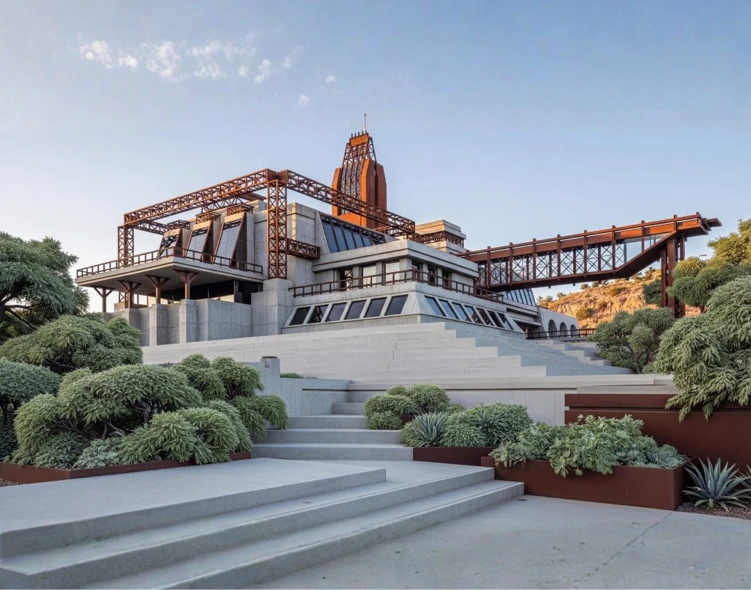 The image shows a modern, architecturally unique building with concrete and metal elements, surrounded by landscaped greenery and steps leading up to the entrance, under a clear sky.