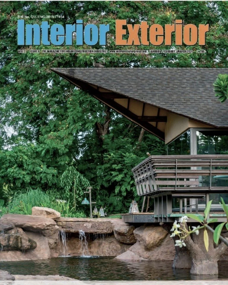Cover of Interior Exterior magazine featuring a modern house with a sloped roof and a balcony, surrounded by lush greenery and a small waterfall with a pond.