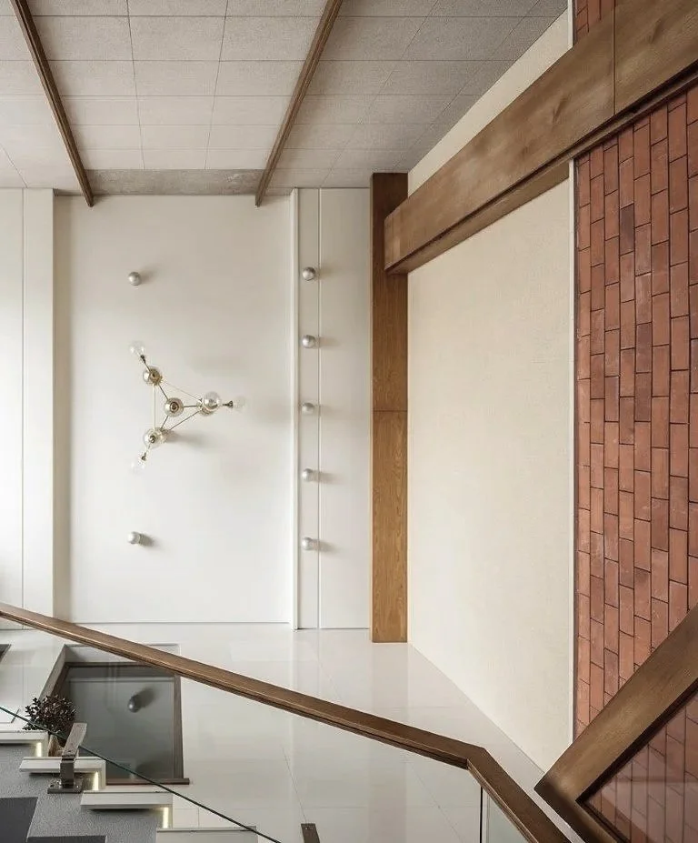 Interior view of a modern building with white walls, a decorative chandelier, and a staircase with wooden handrails.