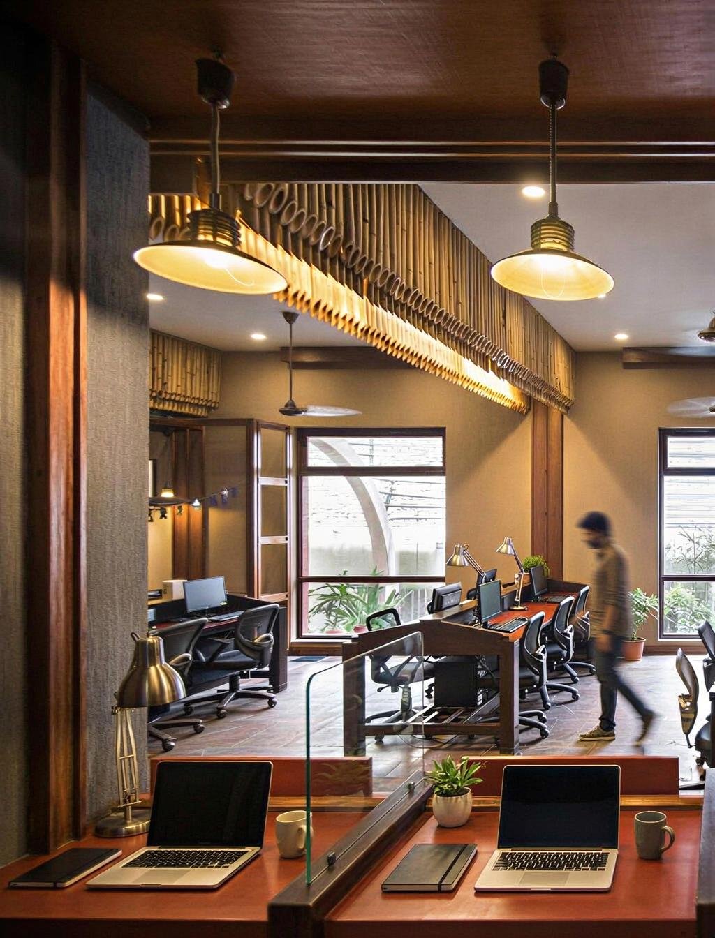 Interior of a modern coworking space with desks, chairs, computers, and large windows. A person is walking past the desks.