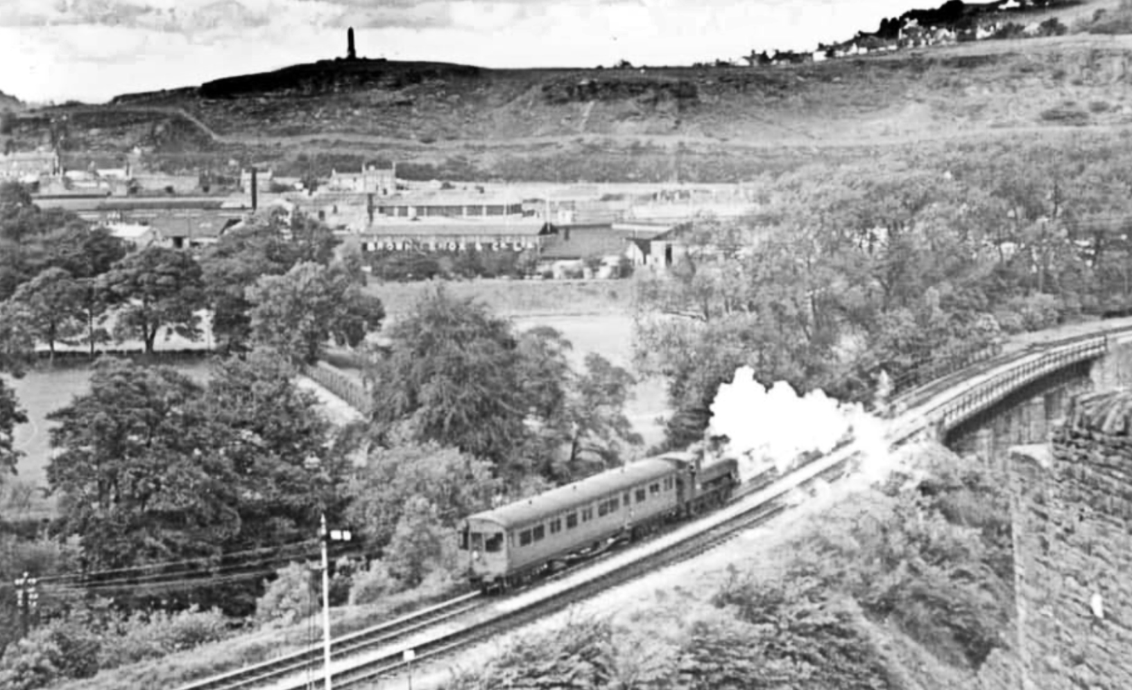 In early BR days, an autotrain drifts southwards away from Pontypridd in the direction of Upper Boat. In the background are the world famous Brown Lenox Chain Works. The well-known photograph of IK Brunel, complete with cigar and stove-pipe hat, standing in front of the anchor chains forged for the ‘Great Eastern’, involved chains made in Pontypridd by Brown Lenox. Acknowledgement: in spite of efforts made to trace its origins, this photo is by a photographer unknown.
