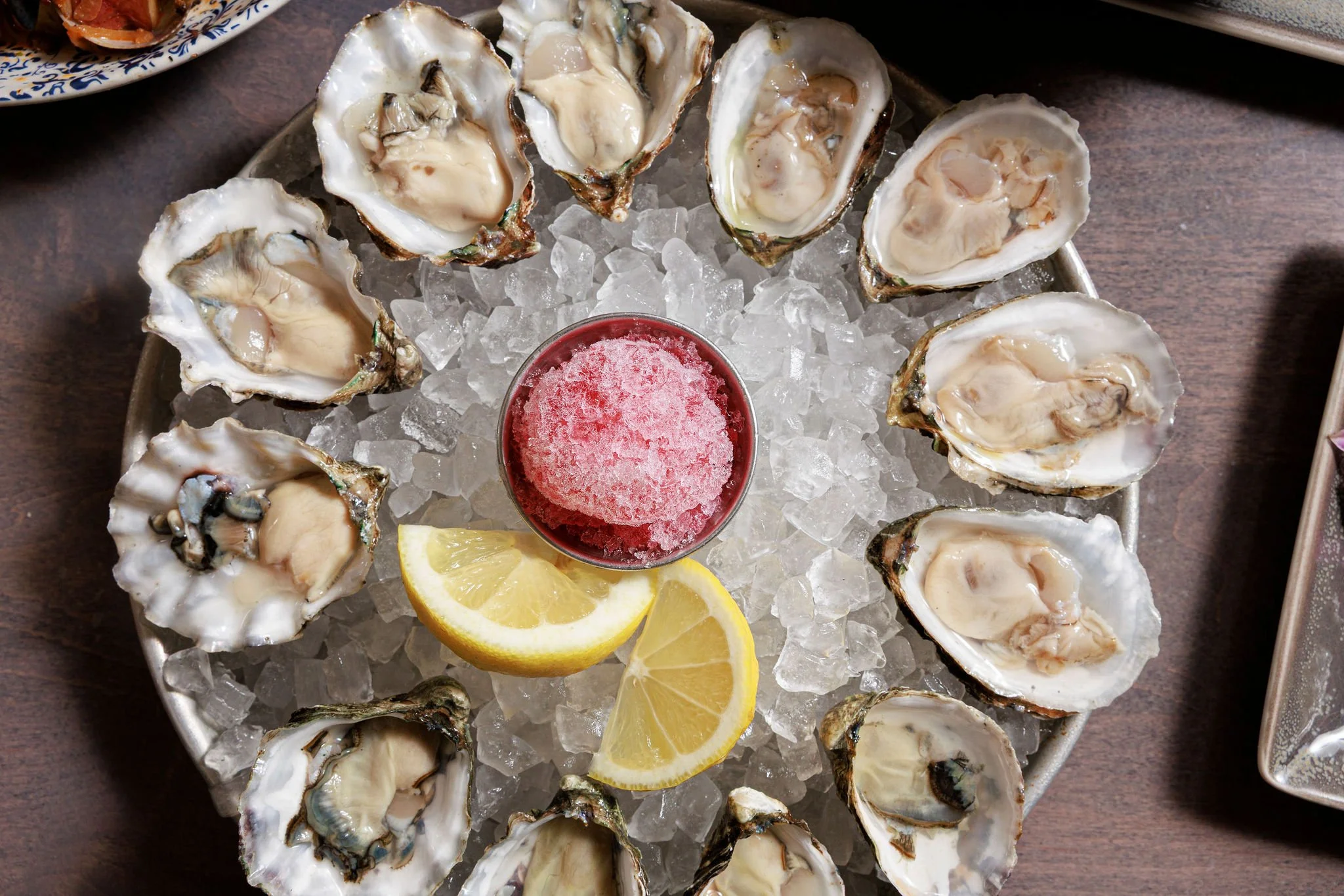 A platter of fresh oysters on ice with lemon wedges and a small container of cocktail sauce.