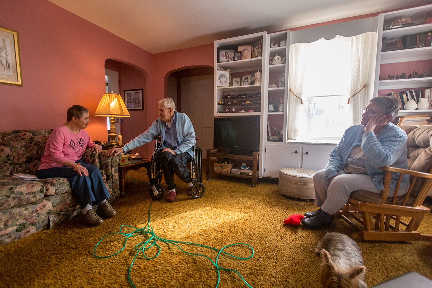  Rollin Lane, 88, sits with Kim, left, his 57-year old daughter with Down Syndrome, and Kris Zamora, right, in his Leominster home. After caring for Kim for her entire life, Rollin’s declining health has forced him to seek assistance with caring for 