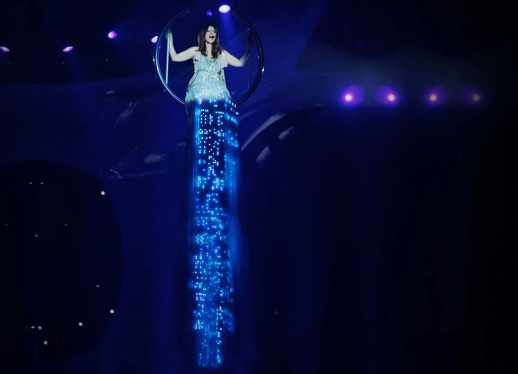 Laura Pausini interprète la chanson Invece no, lors de sa tournée mondiale Inedito, à Milan, le 22 décembre 2011. La chanteuse italienne porte une jupe CuteCircuit de 45 mètres de mousseline de soie incorporant des milliers de leds et cristaux Swarovski.