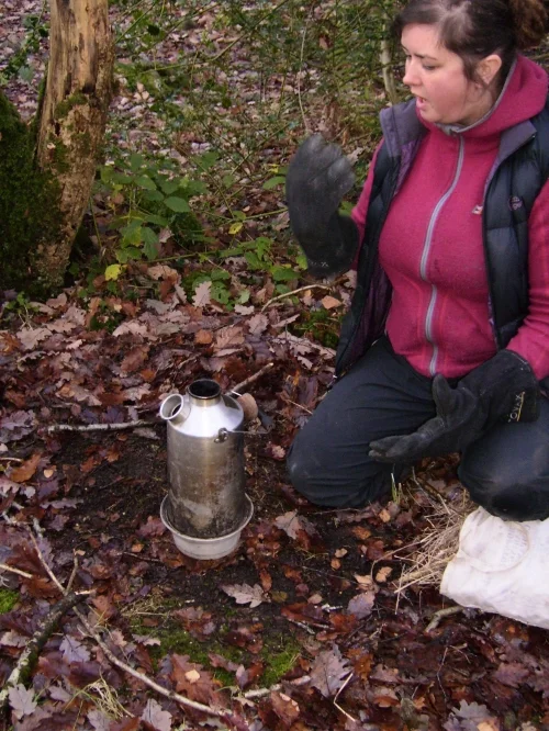 TEA TIME. Note the kneeling position (as modeled by Lily), cork out, established zones with sticks, thermal gloves and flat surface. If you see someone using a storm kettle without this then challenge them - They're not safe and could scold someone!