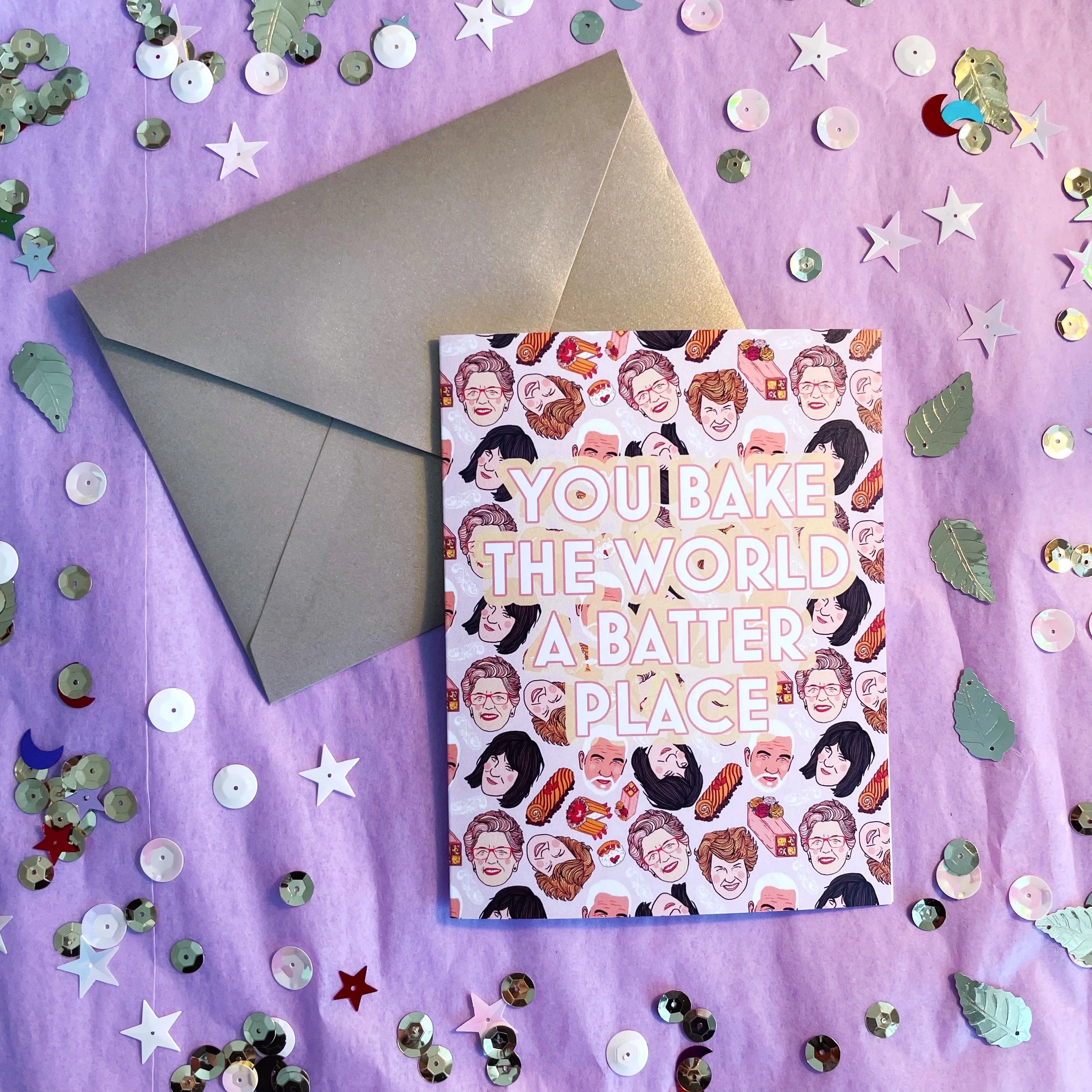 great British baking show patterned greeting card that says you bake the world a batter place with gold envelope on lavender background with gold sequins