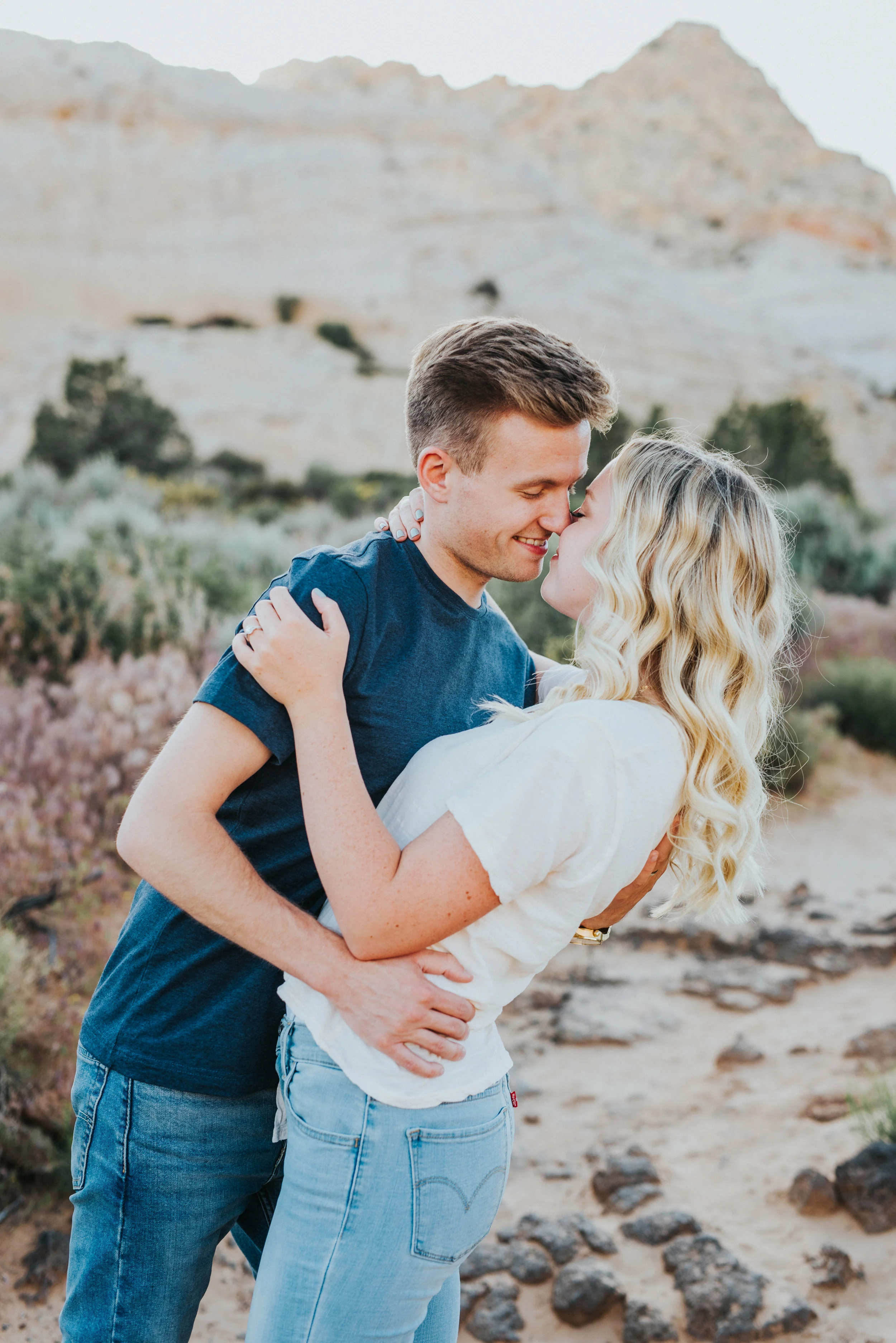  snow canyon engagement session hugging dipping romantic playful kissing northern utah engagement photography saint george utah casual engagement outfits tall grass mountain backdrop  #saintgeorgephotography #snowcanyon #engagementsession #utah #hair