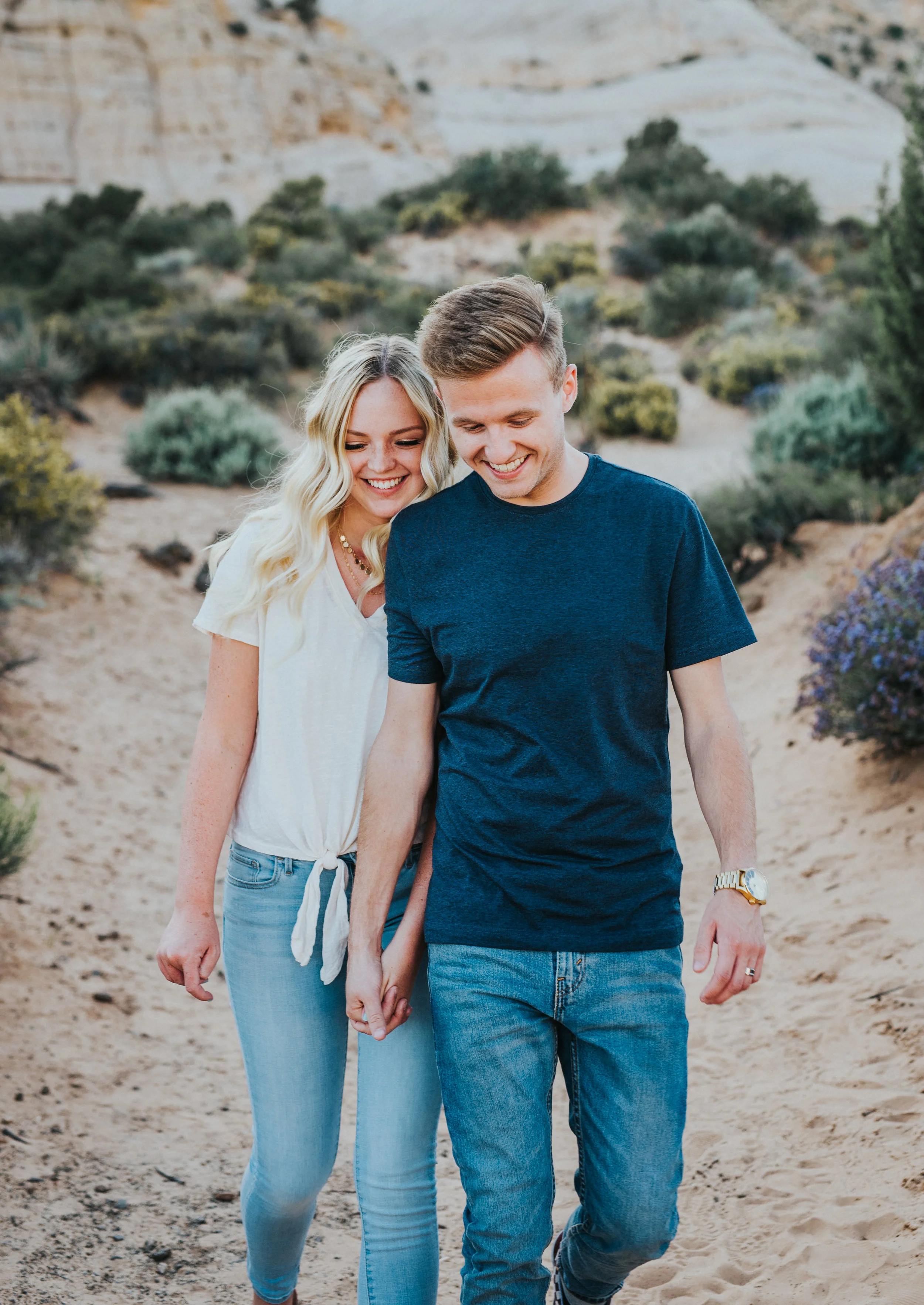  holding hands walking dusty path mountain backdrop casual posing natural candid photography snow canyon utah saint george photographer northern utah photography happy playful engagement session #saintgeorgephotography #snowcanyon #engagementsession 
