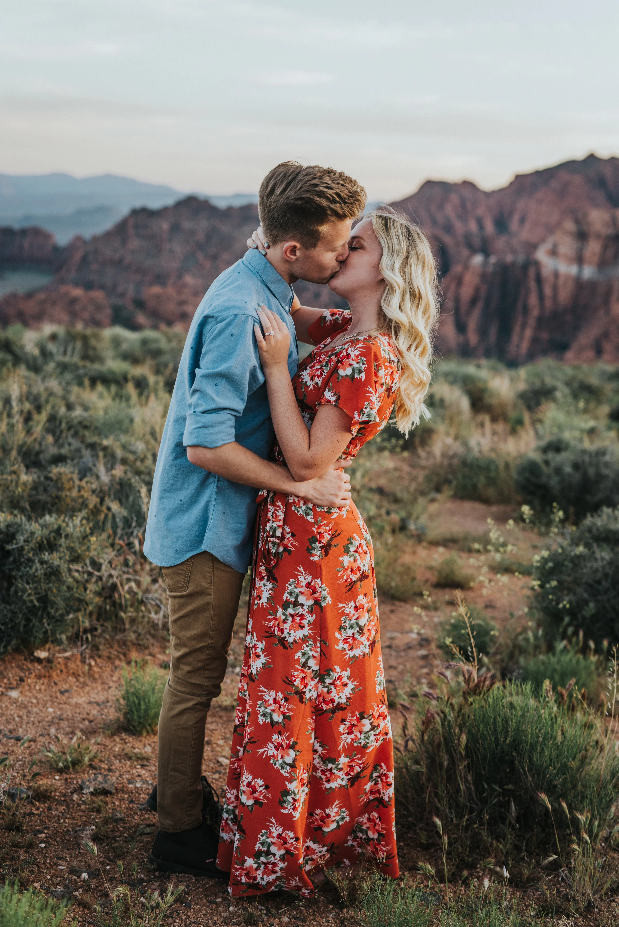  romantic kissing cupping face dipping red rocks mountain backdrop desert snow canyon saint george utah photographer blonde hair inspiration tall grass hugging #saintgeorgephotography #snowcanyon #engagementsession #utah #hairinspiration #outfitinspo