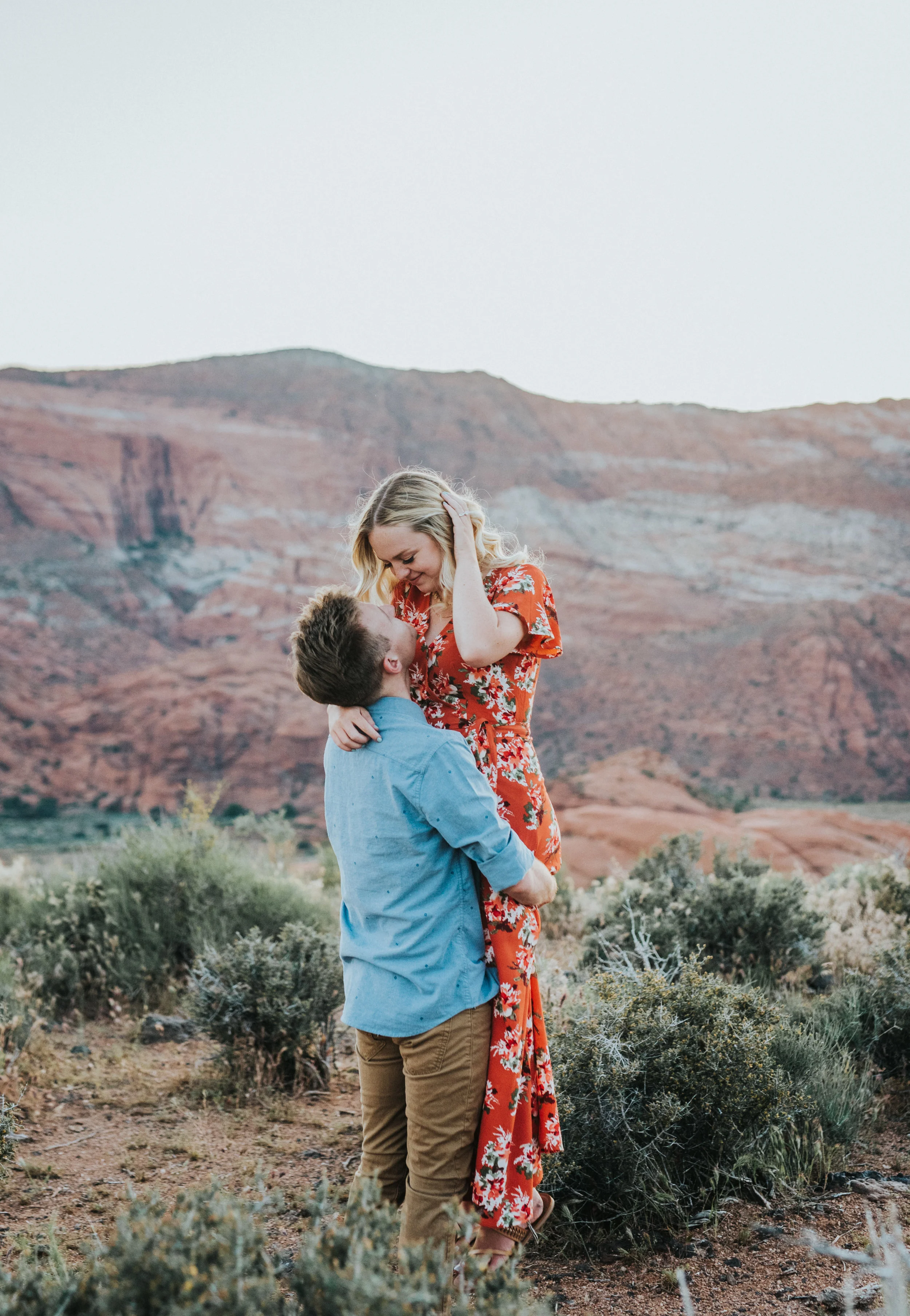  brushing hair out of face tucking hair behind ear romantic happy smiling holding fiance red rock engagement session snow canyon saint george utah engagement photography sunset mountains #saintgeorgephotography #snowcanyon #engagementsession #utah #h