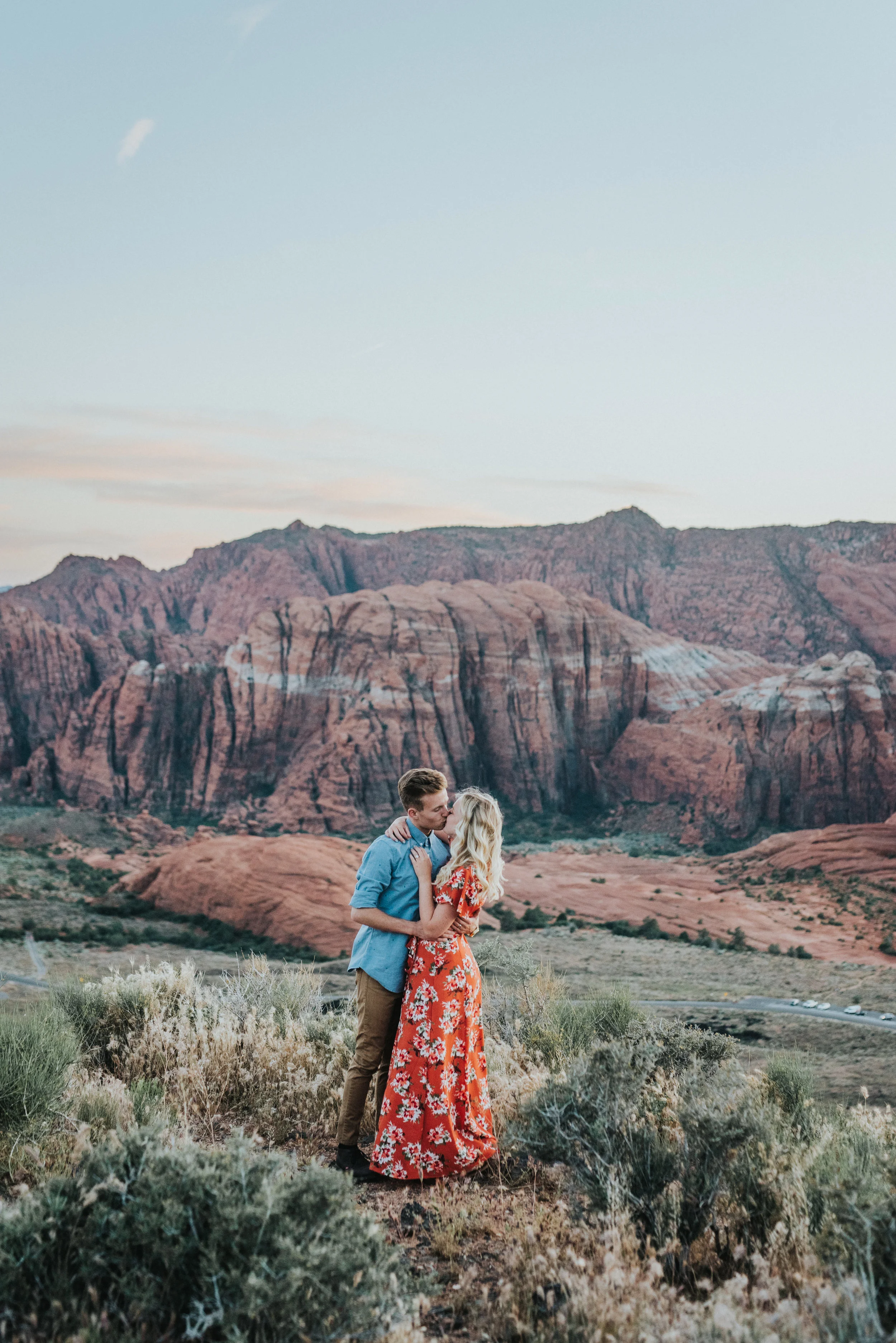  hugging kissing overlooking red rock mountains saint george engagement session snow canyon desert romantic authentic posing northern utah photographer floral long dress modest #saintgeorgephotography #snowcanyon #engagementsession #utah #hairinspira