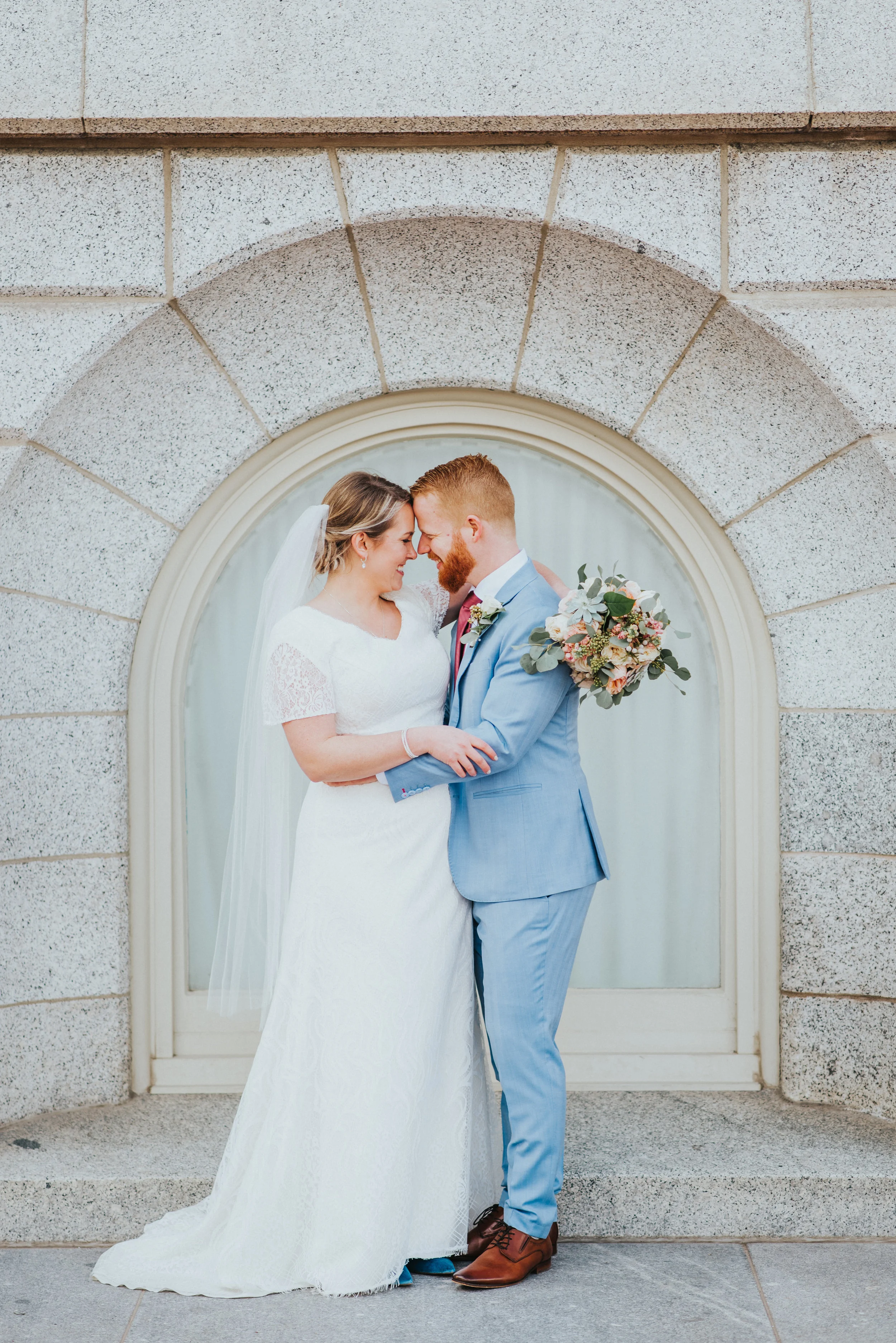  northern utah professional wedding photographer salt lake city temple wedding lds temple grounds couple photos hugging smiling long veil modest wedding dress blue powdered suit red wedding tie pastel bouquet #northernutahweddingphotographer #saltlak