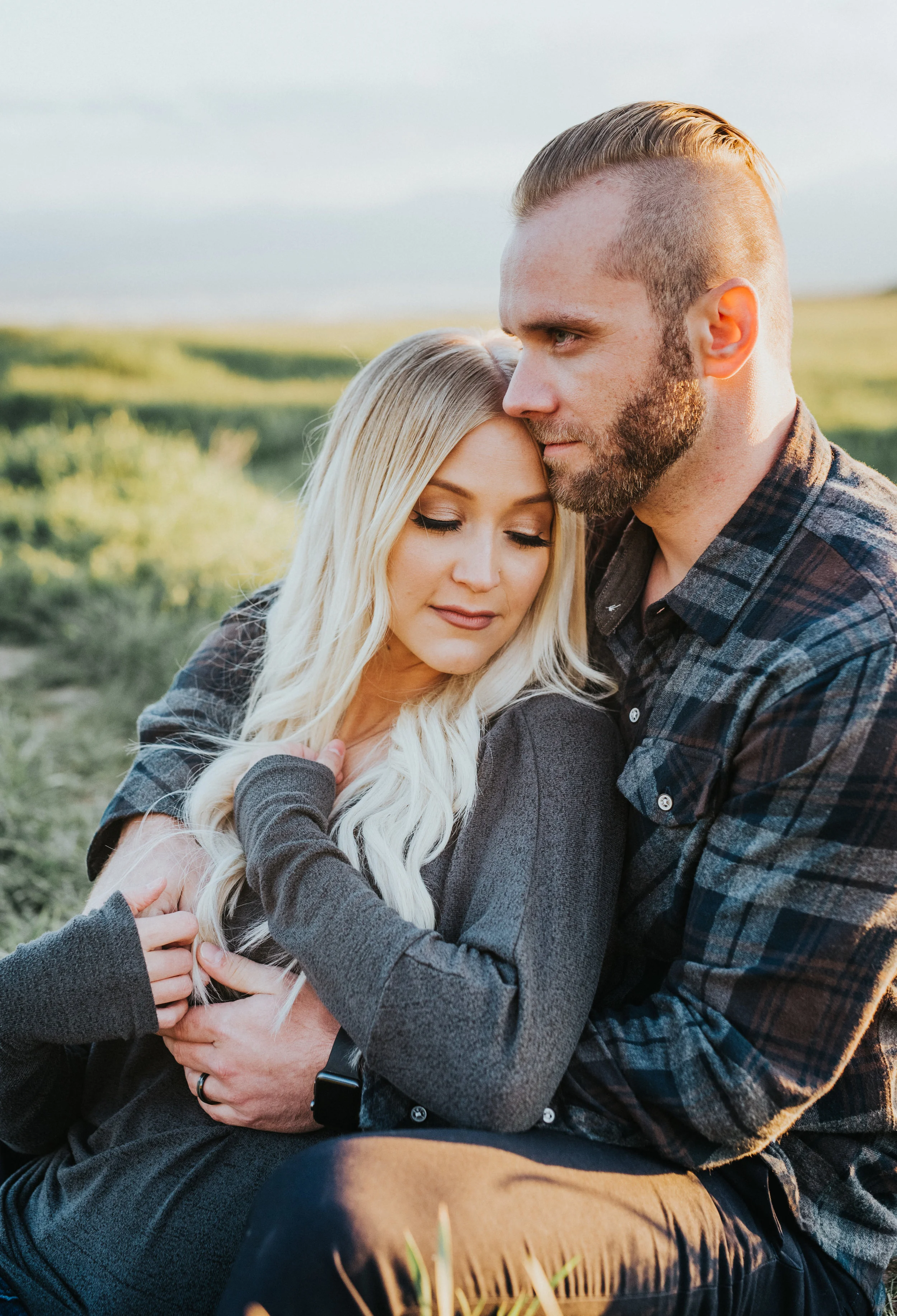  true to color photography tunnel springs engagement photography northern utah photographer fall colored outfit inspiration sitting hugging playful green field mountain background blue skies hair inspiration blonde faded haircut #engagementphotograph
