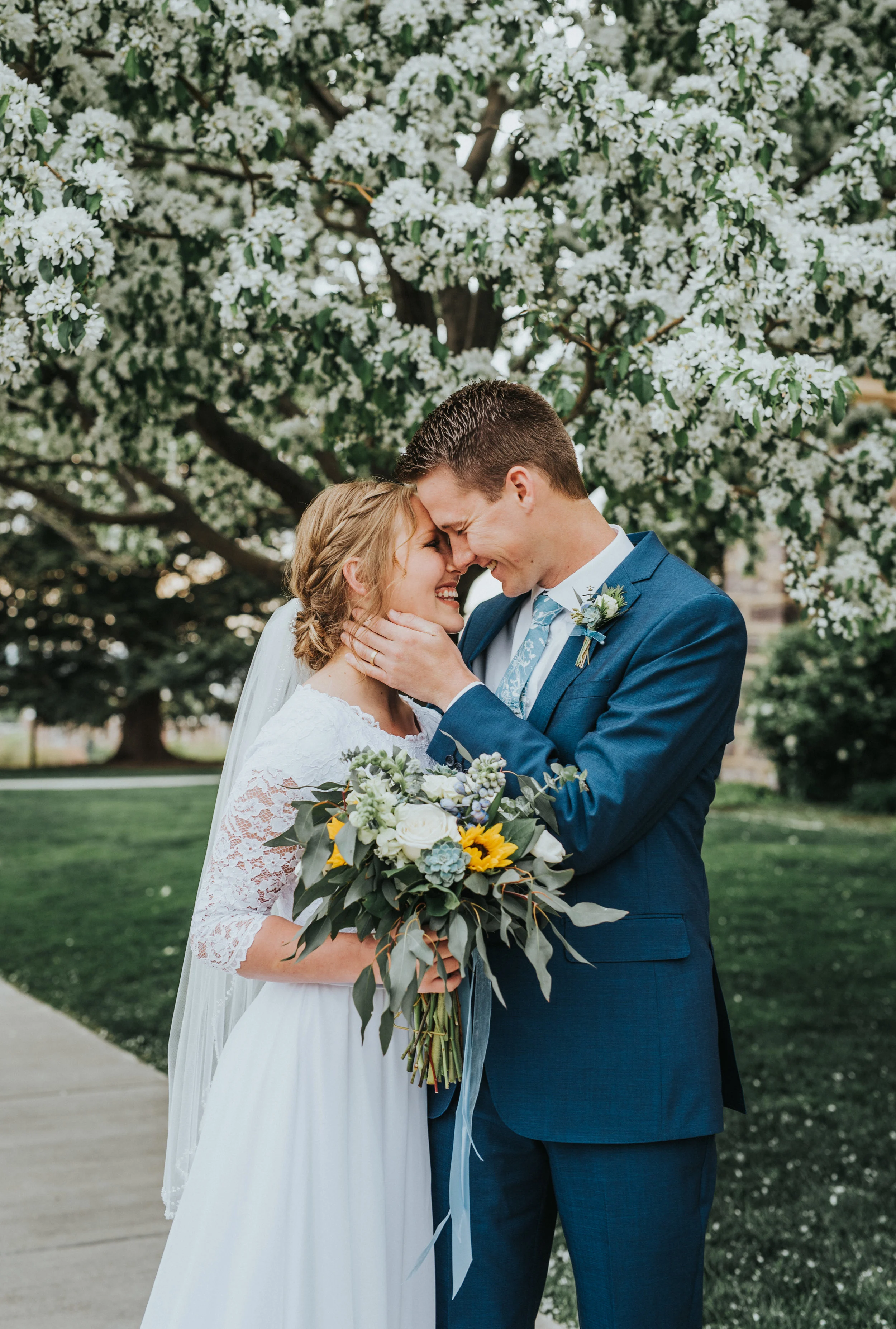  spring wedding blossoming trees hugging playful romantic posing touching cheek foreheads touching messy sunflower and blue and white floral wedding bouquet logan utah temple wedding grounds best cache valley photographer #Loganutah #cachevalleyphoto