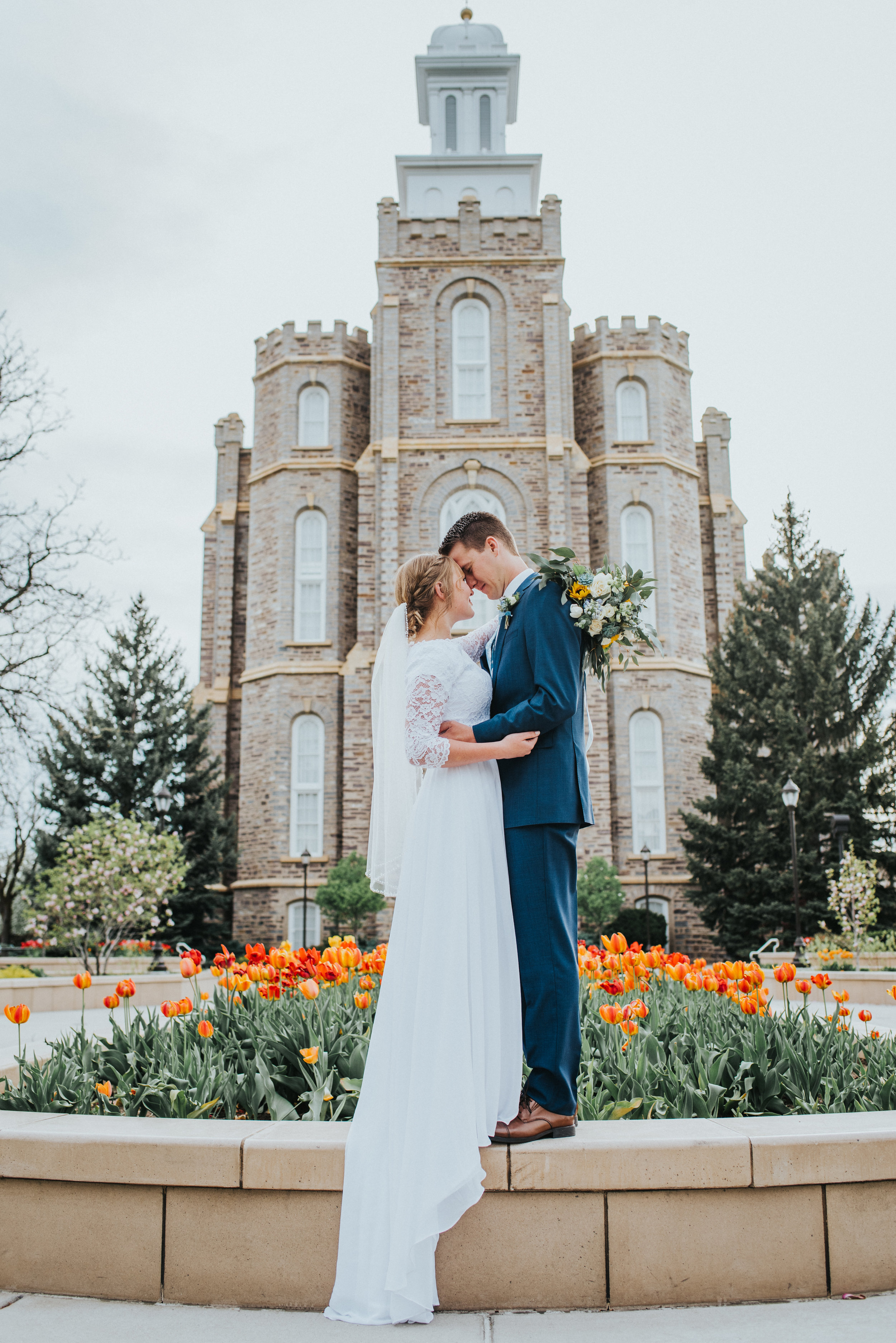  logan utah lds temple wedding grounds spring wedding orange and red tulips hugging foreheads touching romantic wedding photos wedding train lace modest wedding gown holding bouquet sunflower blue and white wedding bouquet best cache valley wedding p
