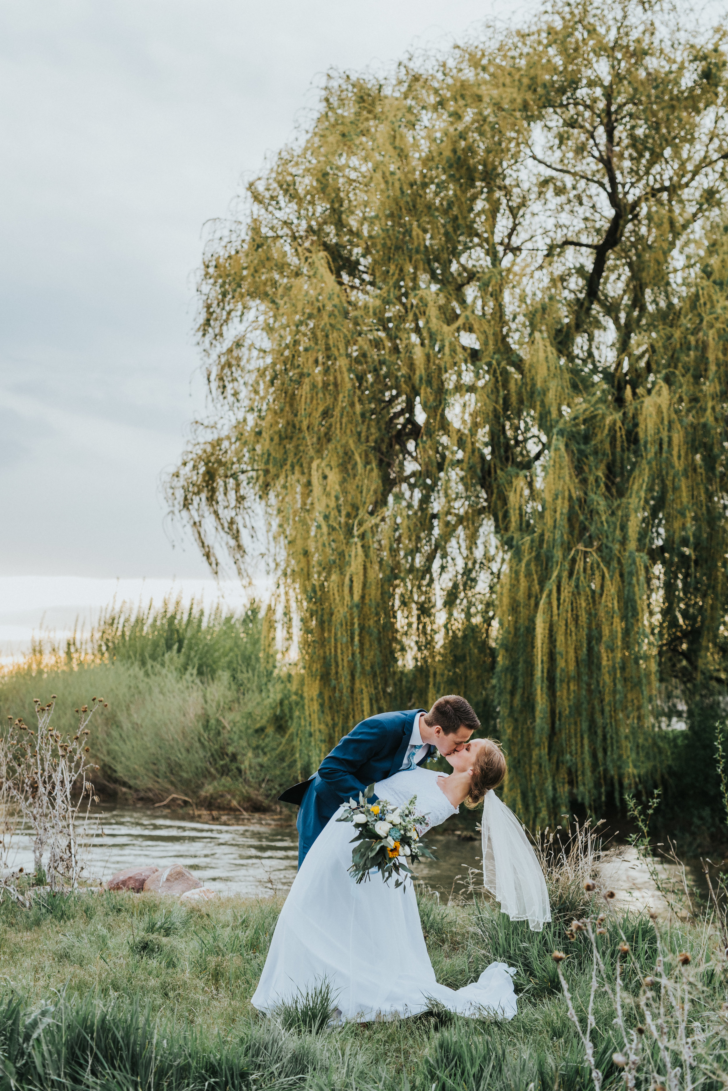  overcast sunset romantic passionate dipping kissing billowy short wedding veil stream willow tree overgrown grass candid photography logan utah photography locations cache valley utah professional best wedding photographer #Loganutah #cachevalleypho