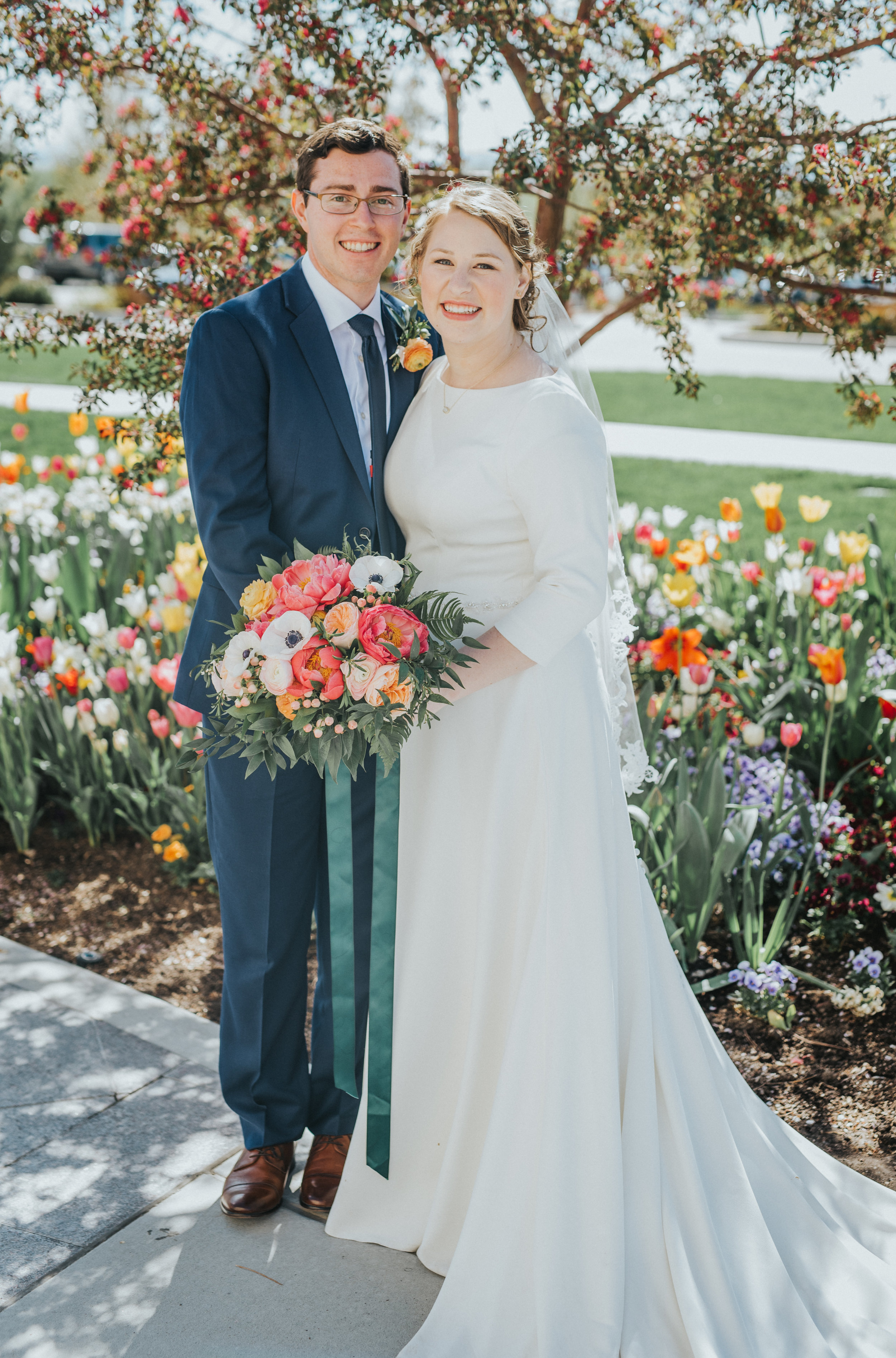  spring wedding tulips payson utah lds temple wedding grounds hugging holding hands bride and groom just married poppy pink and peach floral wedding bouquet emerald green bouquet ribbon modest wedding dress navy wedding suit best payson utah photogra