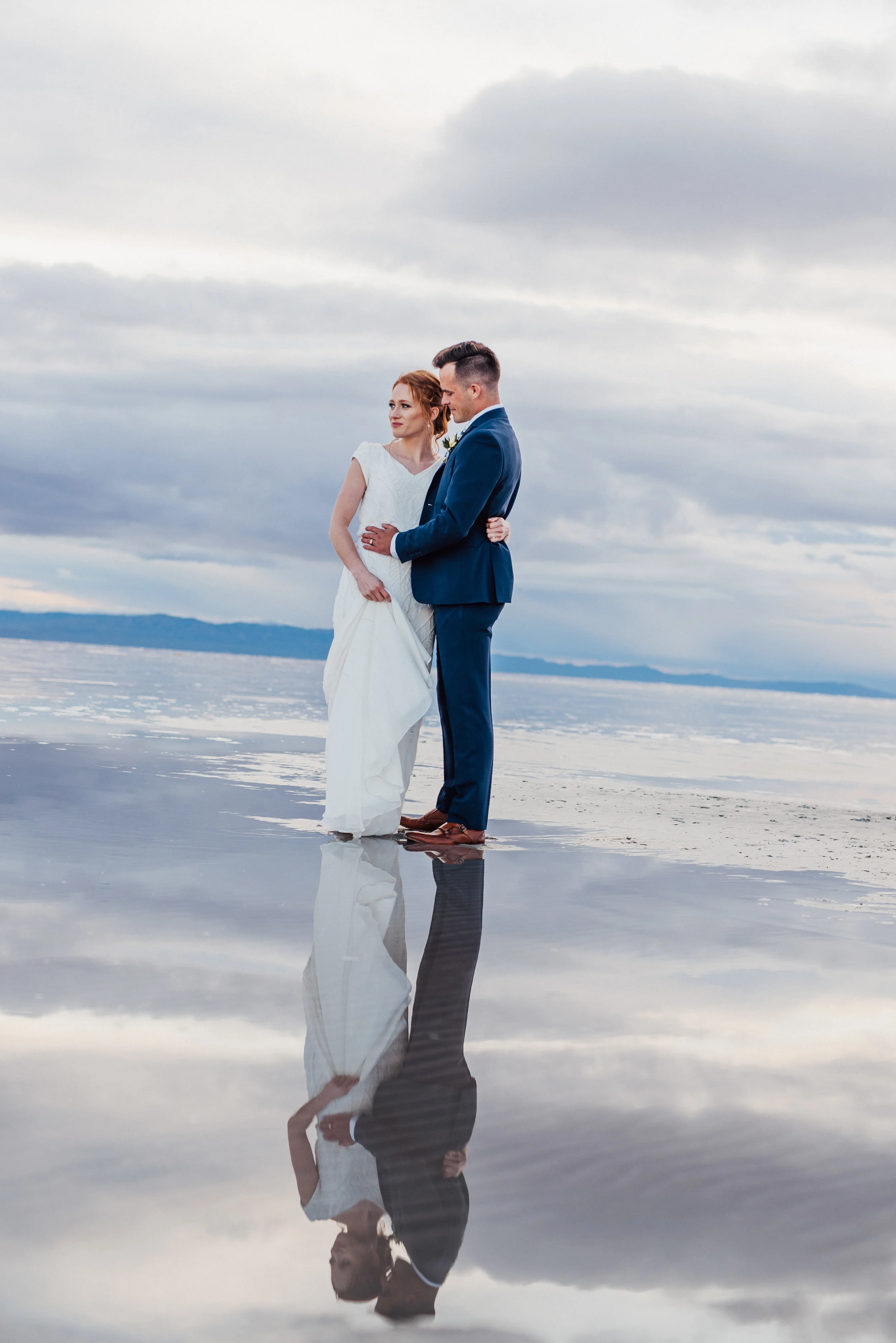  cloudy water reflections dramatic formal bridals hugging looking into the distance modest white wedding dress wet wedding dress mountain backdrop northern utah wedding photographer #spiraljetty #saltlakecityweddingphotographer #saltlake #ido #northe