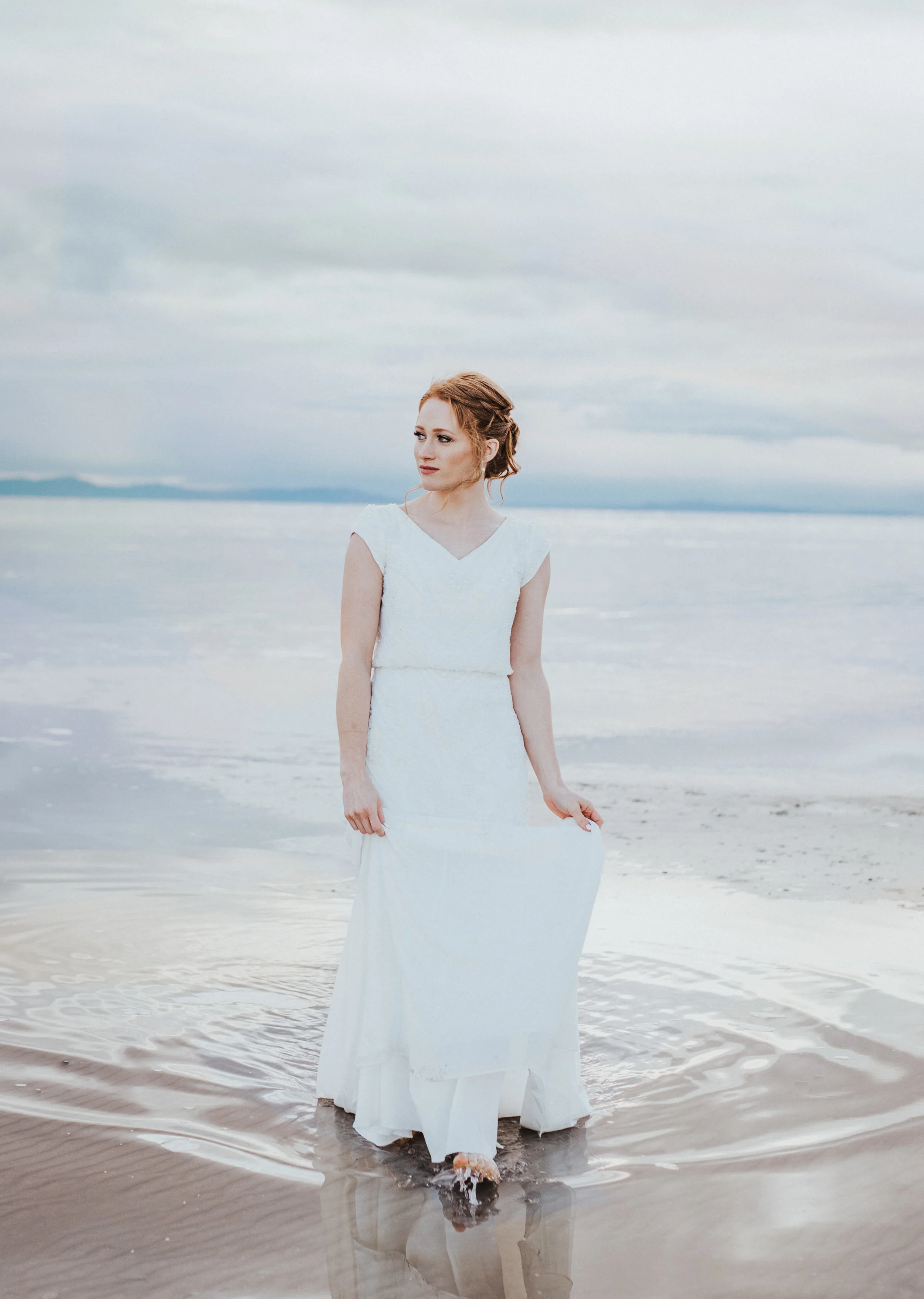  bride walking in water wet wedding train red hair bridal updo inspiration sunset bridal session the great salt lake cloudy sky moody skies looking into distance best northern utah wedding photographer #spiraljetty #saltlakecityweddingphotographer #s