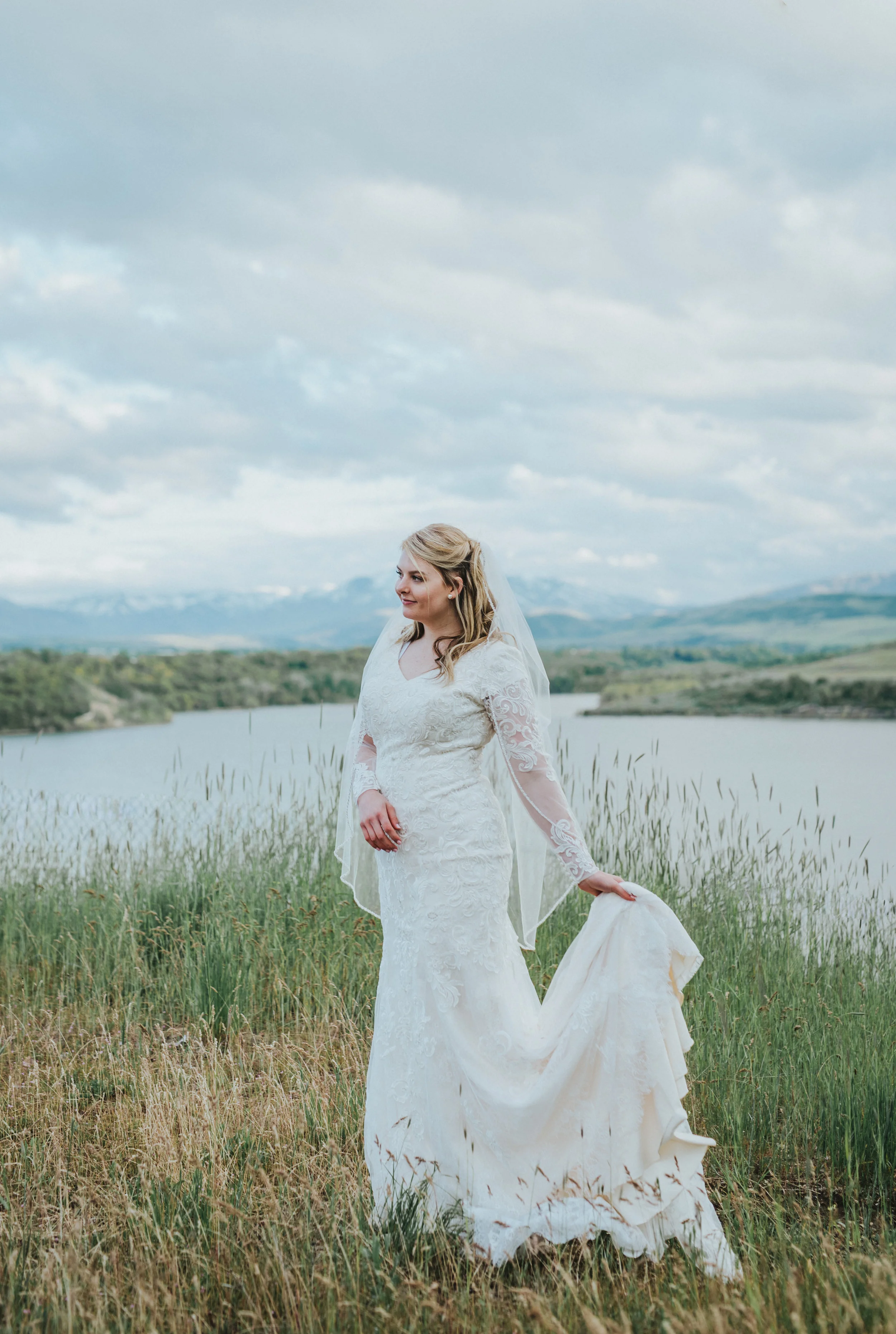  bridal photos holding wedding train bohemian hyrum reservoir logan utah cache valley northern utah wedding photographer tall grass mountain water backdrop bride to be pearl earrings #cachevalleyutah #hyrumutah #northernutahphotographer #bridals #hyr