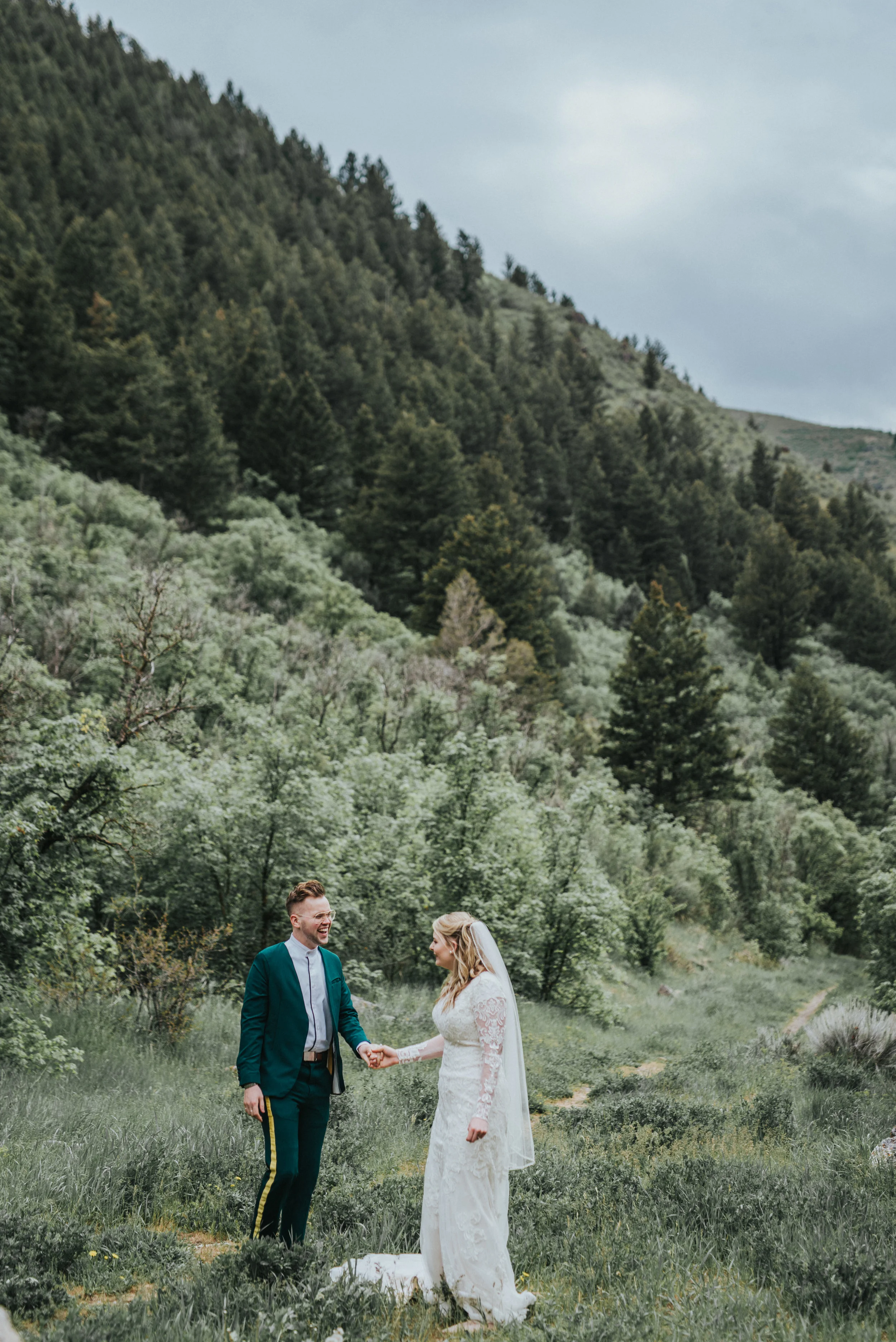  green mountain background tall trees holding hands walking grass eerie skies formal photography northern utah wedding photographer hyrum reservoir #cachevalleyutah #hyrumutah #northernutahphotographer #bridals #hyrumreservoir #blacksmithforkcanyon #