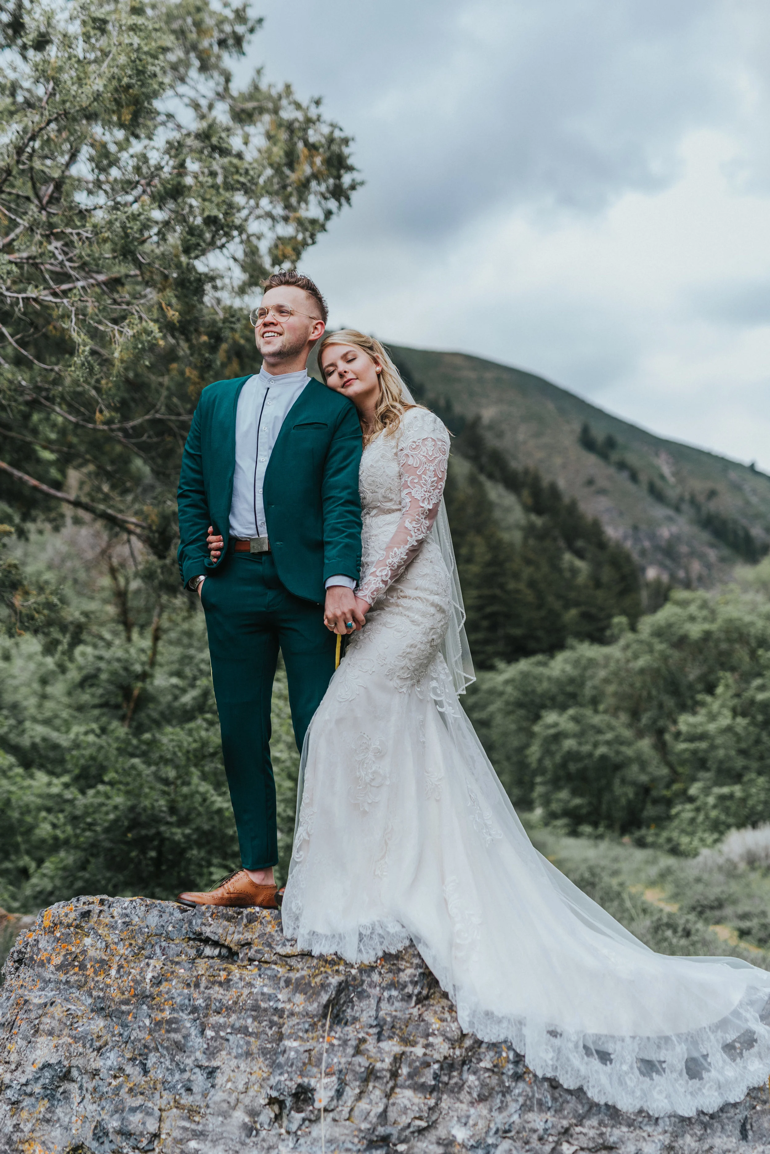 long lace wedding train green wedding suit retro yellow striped pants vintage glasses holding hands romantic mountain backdrop cloudy skies northern utah wedding photographer logan utah cache valley #cachevalleyutah #hyrumutah #northernutahphotograp