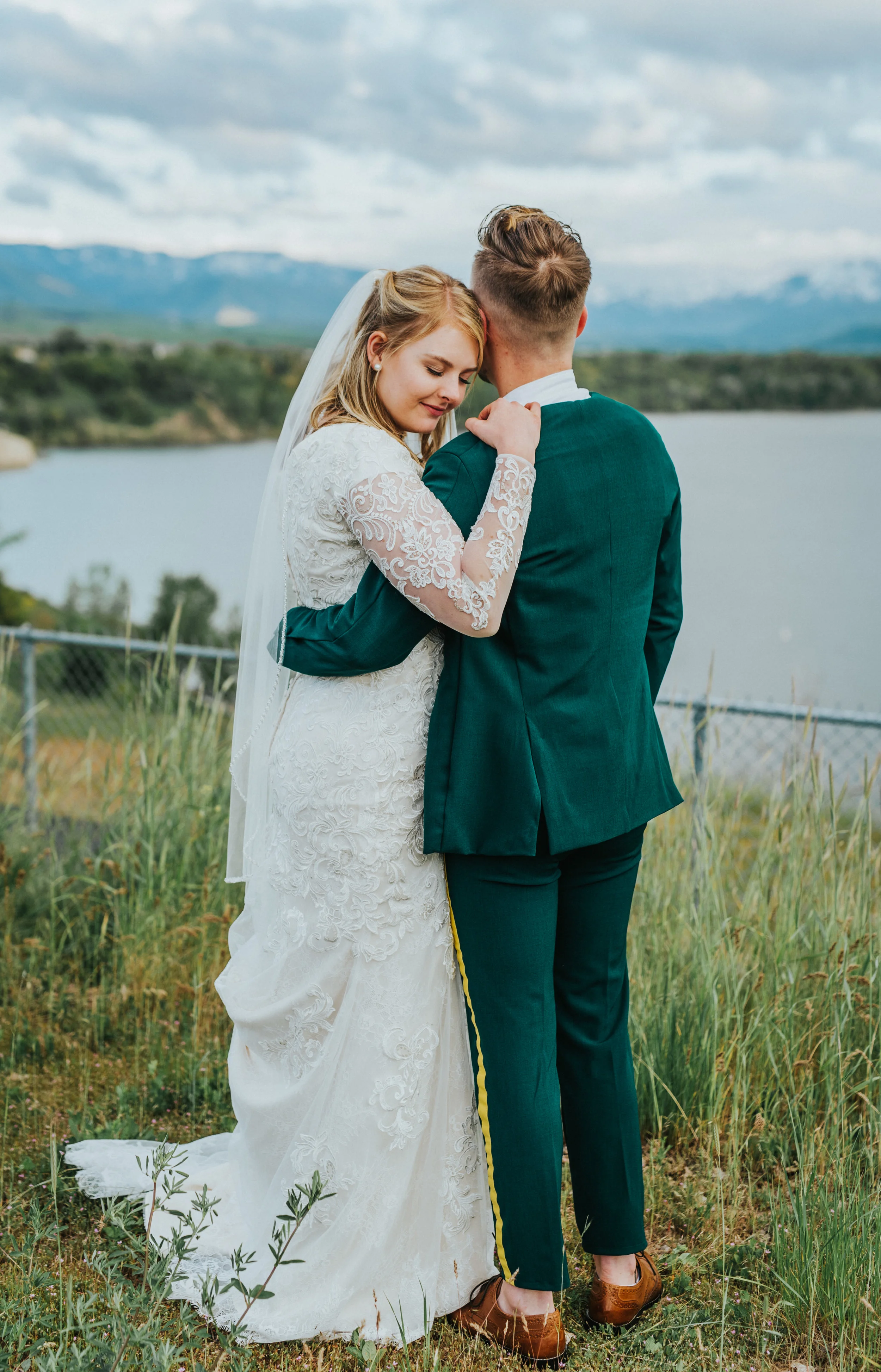  hyrum reservoir utah water hugging standing profile pictures sunset mountain scenery emerald green wedding suit lace wedding dress modest northern utah wedding photographer romantic outdoor wedding #cachevalleyutah #hyrumutah #northernutahphotograph