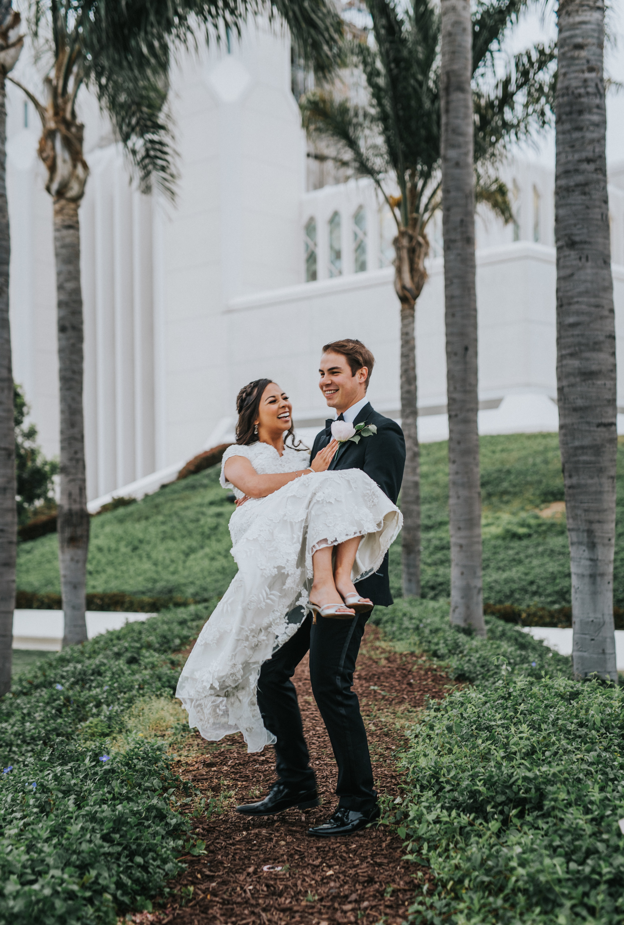  hugging groom holding bride laughing smiling happy temple grounds san diego lds temple wedding northern utah wedding photographer lace modest wedding dress #lajollacaliforniaweddingphotographer #sandiegotemple #windanseabeachcalifornia #northernutah