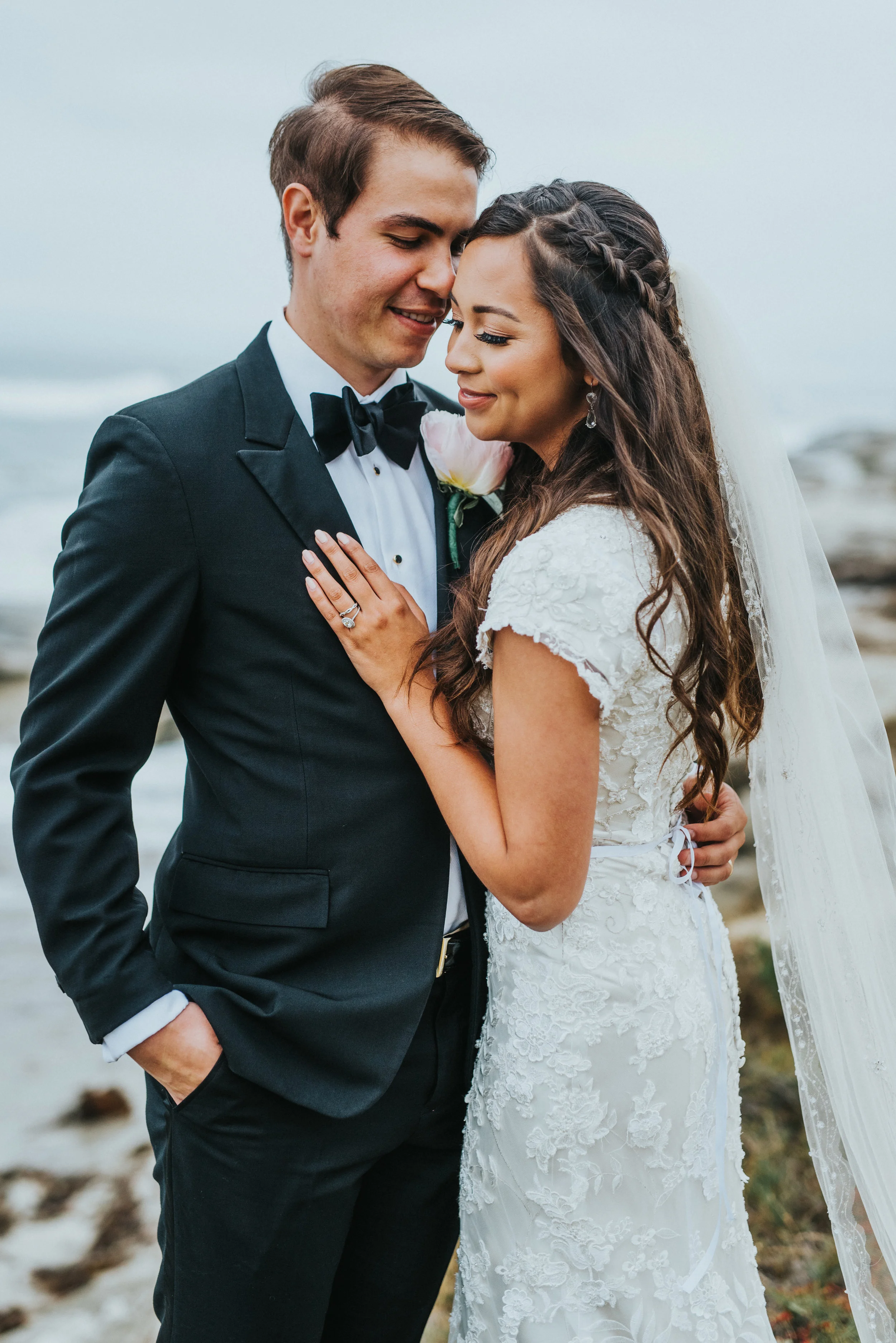  windansea beach la jolla california bridal session hugging smiling romantic overcast beach cliffs hand on chest lace beaded modest wedding dress northern utah wedding photographer #lajollacaliforniaweddingphotographer #sandiegotemple #windanseabeach