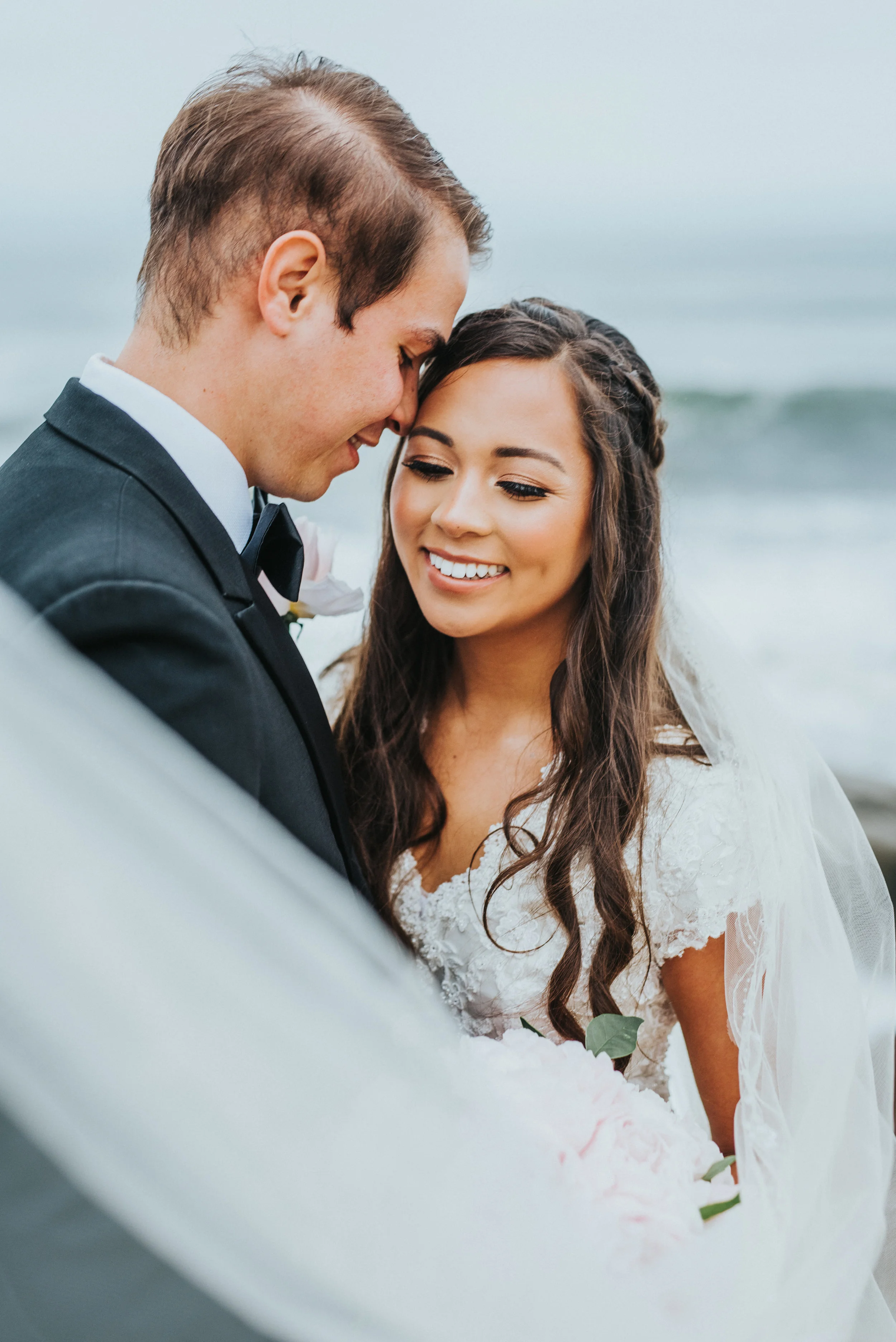  bridal hair inspiration loose curls braids modest cap sleeve lace beaded wedding dress windy bridal veil overcast beach san diego california northern utah wedding photographer natural wedding makeup #lajollacaliforniaweddingphotographer #sandiegotem