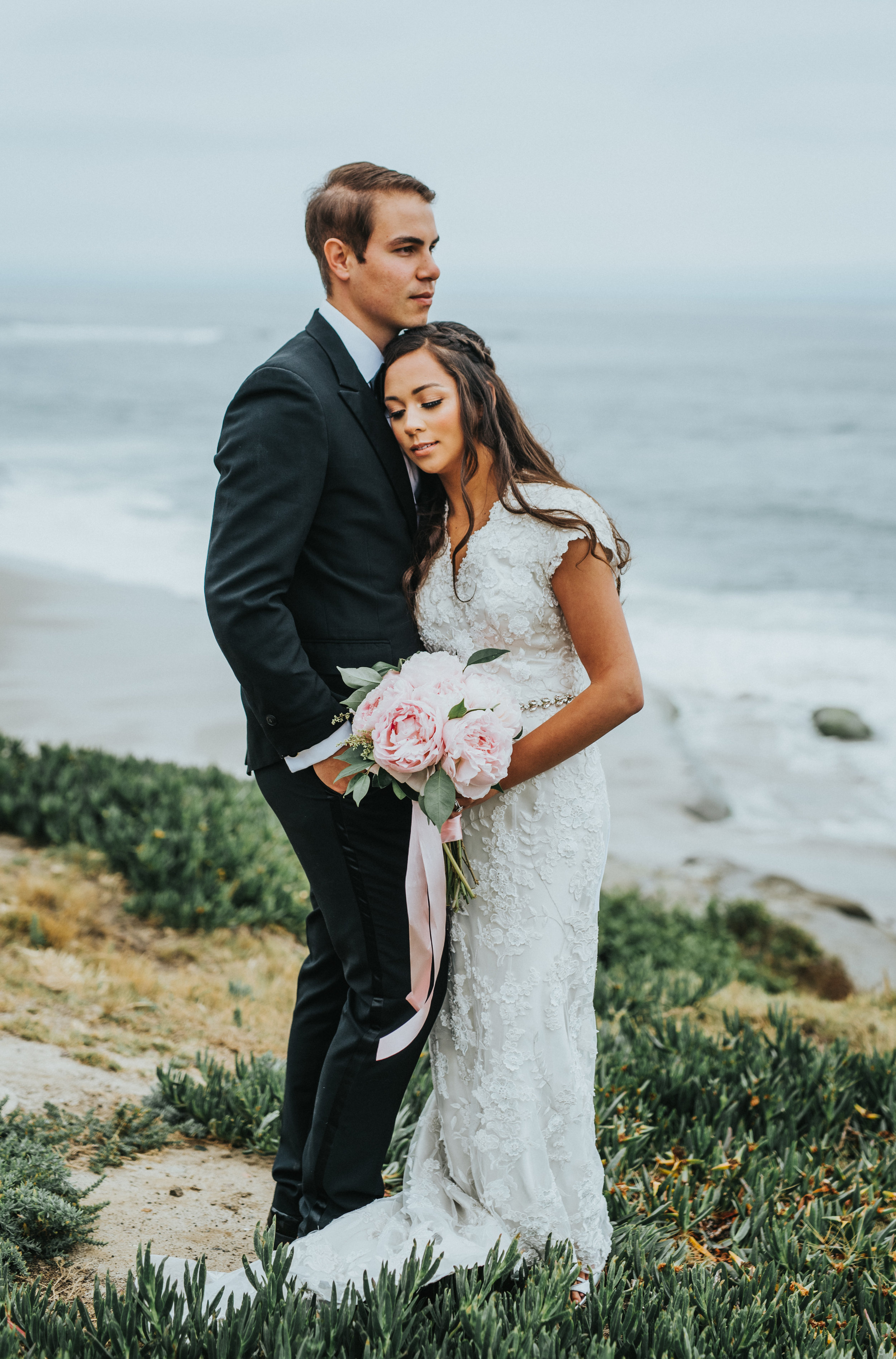  head on shoulder romantic snuggling cliffs overcast skies san diego california windansea beach northern utah wedding photography romantic lace wedding dress beaded dress sash #lajollacaliforniaweddingphotographer #sandiegotemple #windanseabeachcalif