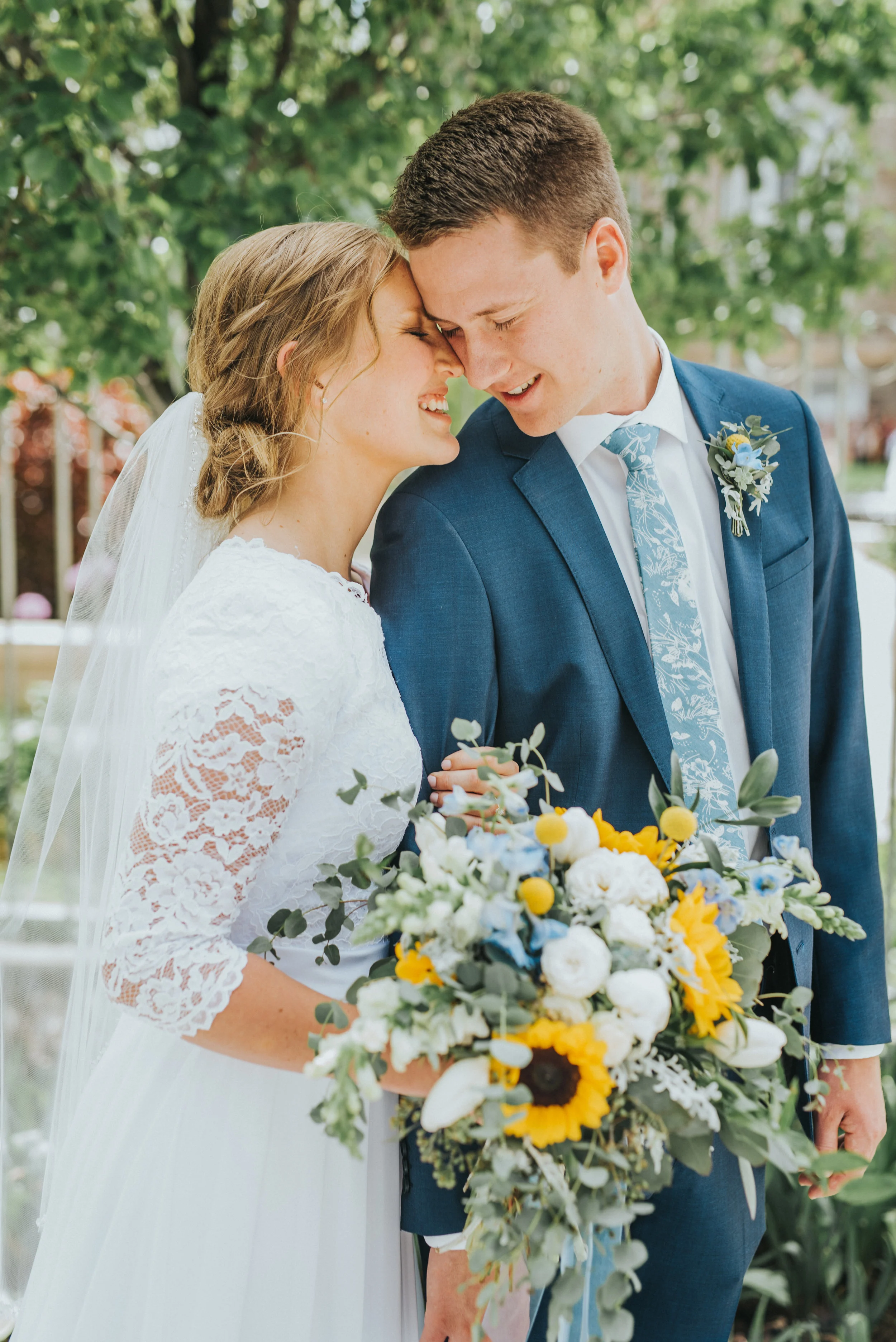  three quarter length lace sleeved wedding dress braided messy updo blue wedding tie sunflower wedding bouquet loose floral arrangement logan utah professional wedding photographer old rock church smiling authentic posing foreheads touching #Loganuta