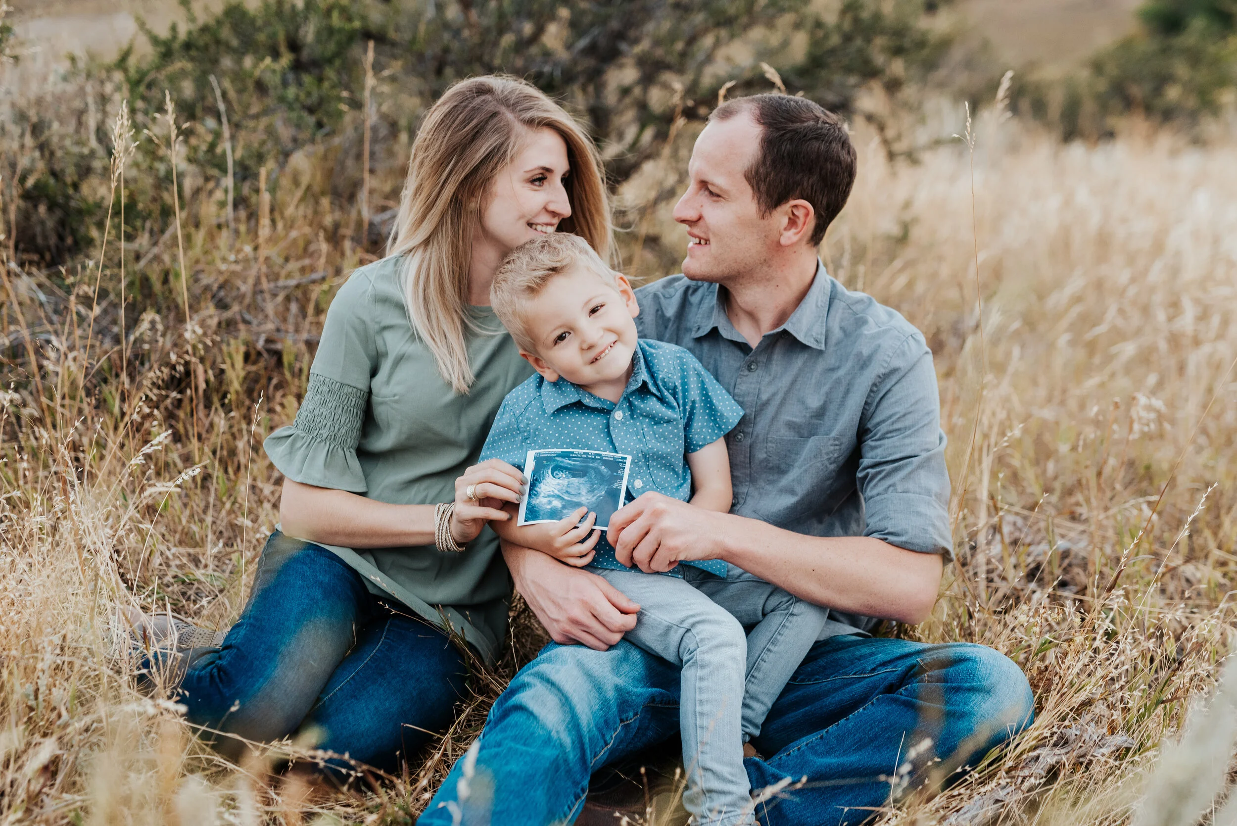 Mother and father smiling at each other while they hold their son and an ultrasound picture. baby announcement in family portraits in logan utah cache valley photographers in northern utah professional photographers in utah family pose inspiration c…