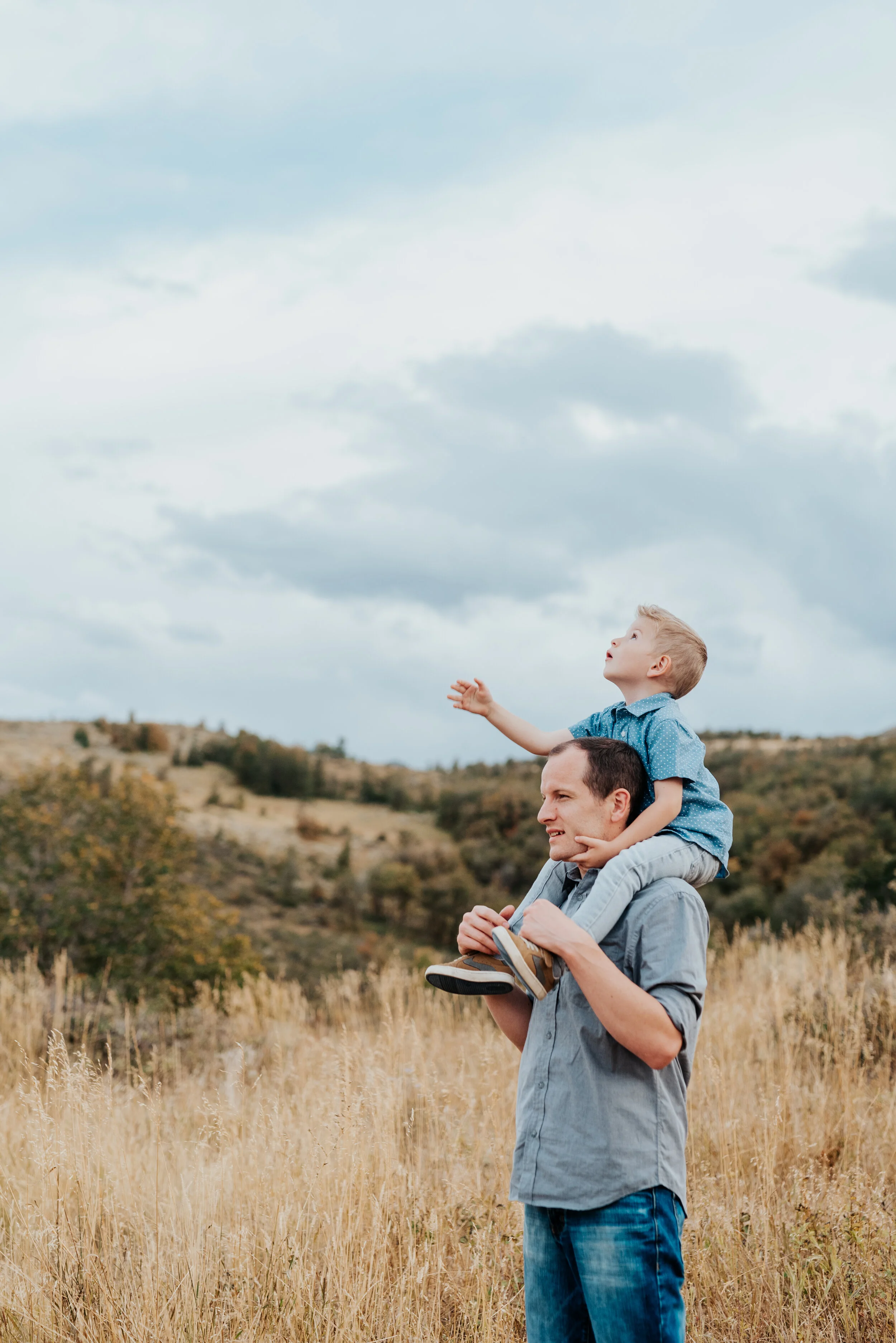  Dad carrying his young son on his shoulders through a golden field in beautiful Cache Valley. parent and children poses baby announcement in family portraits in logan utah cache valley photographers in northern utah professional photographers in uta