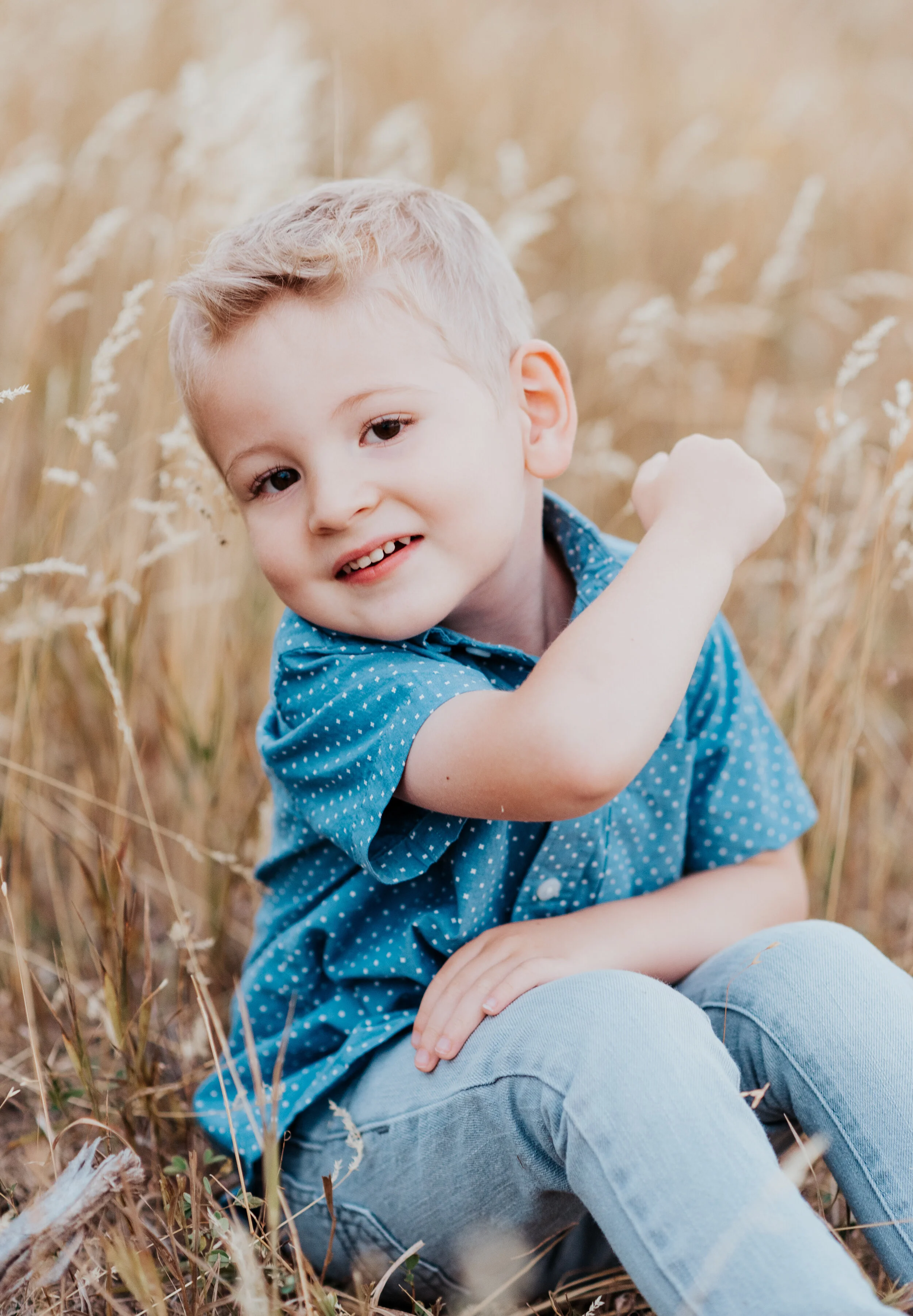  Blonde young boy sitting and playing in a wheat field in a blue shirt and jeans. casual outfit styles sweet parent and children poses baby announcement in family portraits in logan utah cache valley photographers in northern utah professional photog