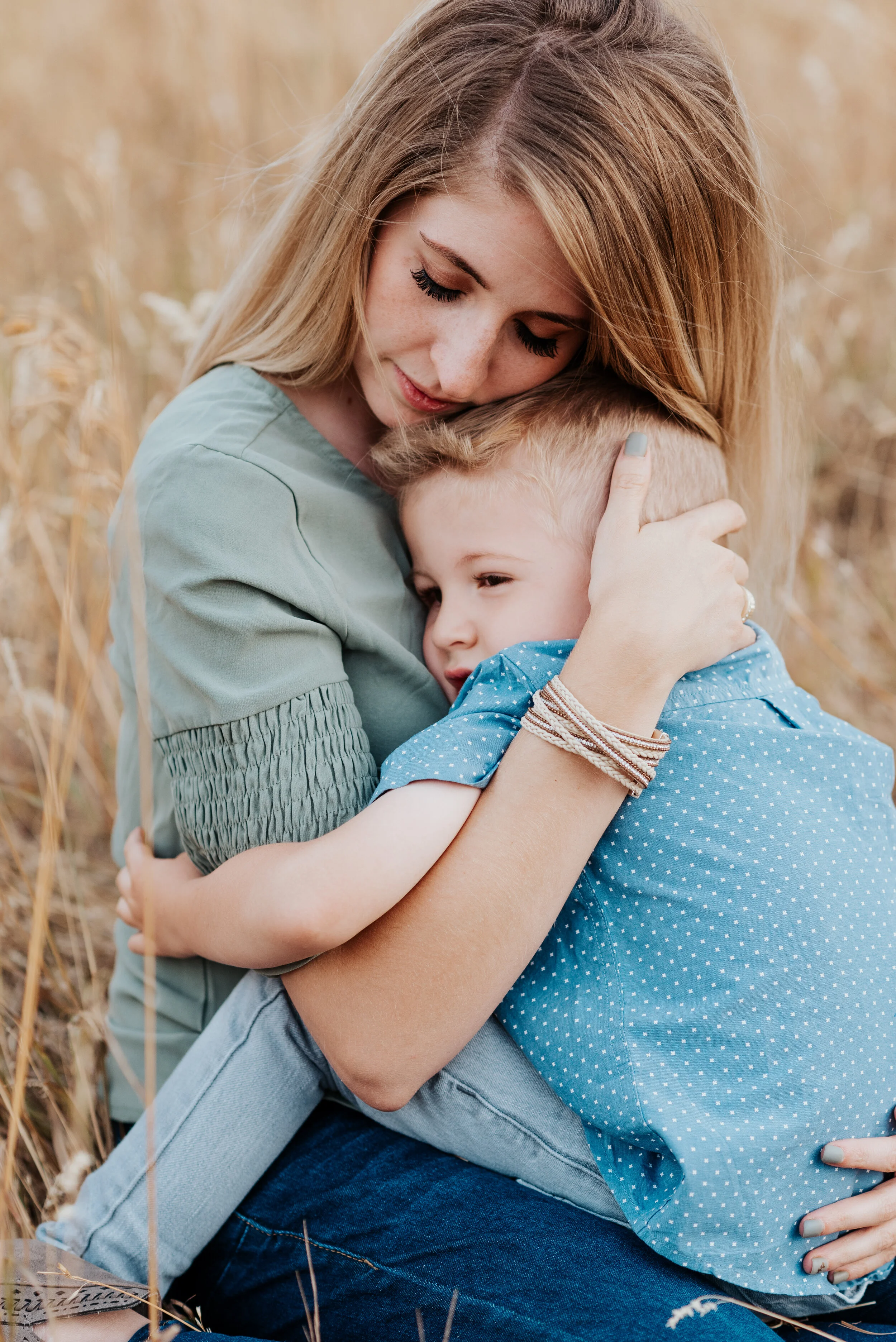  Mom sitting in a field of yellow grass hugging her son close. sweet parent and children poses baby announcement in family portraits in logan utah cache valley photographers in northern utah professional photographers in utah family pose inspiration 