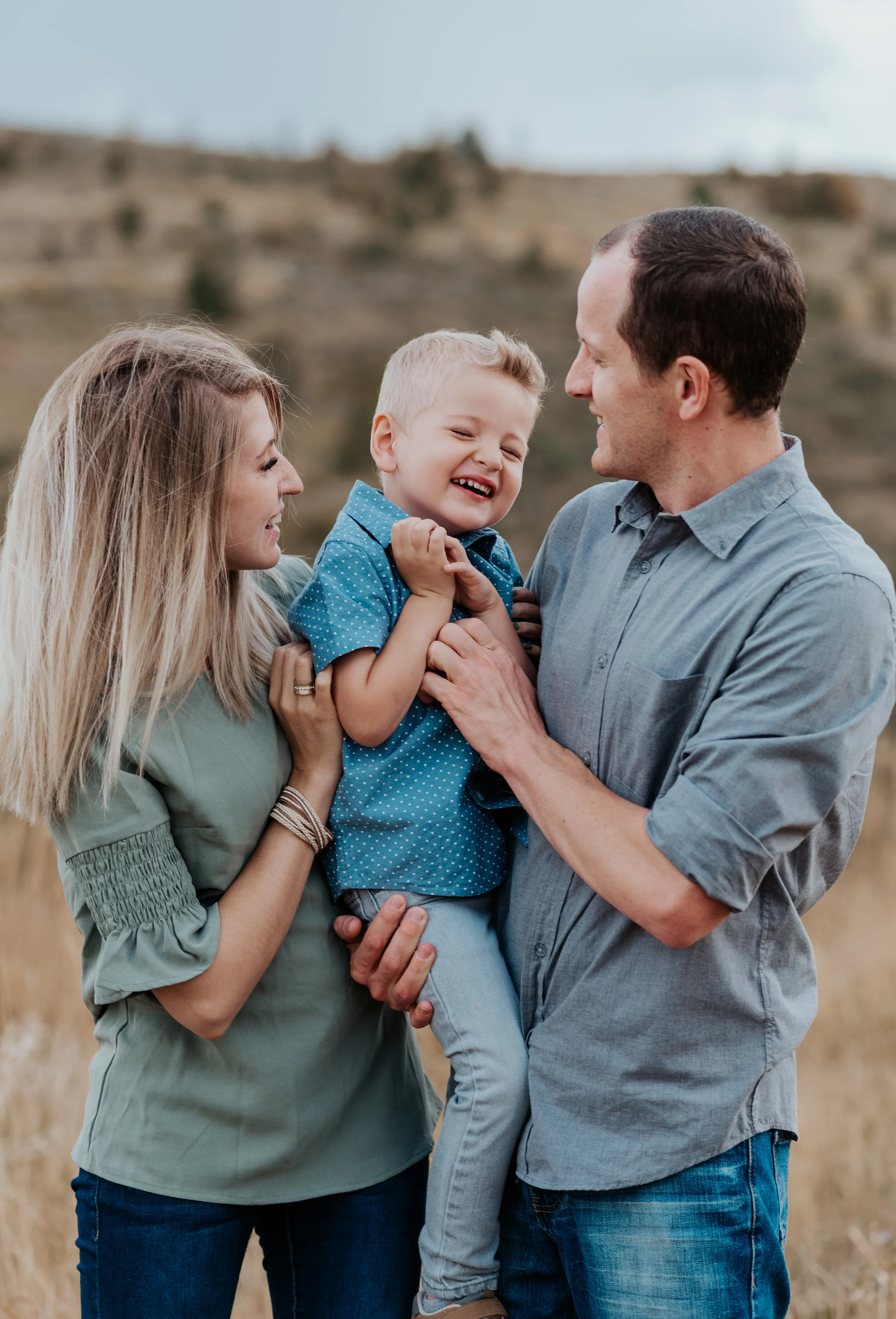 Mother and father holding their cute little boy in their arms in Cache Valley. casual outfit styles sweet parent and children poses baby announcement in family portraits in logan utah cache valley photographers in northern utah professional photogra