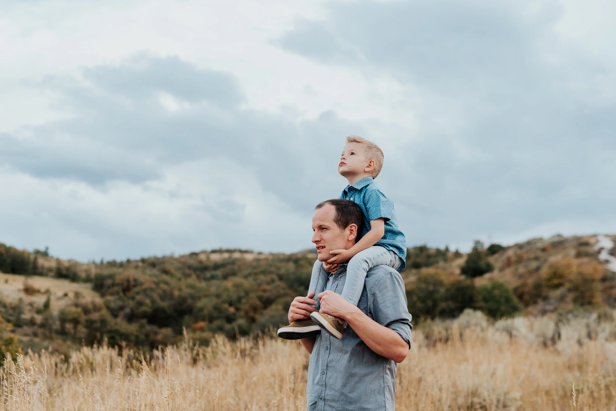 Dad carrying his young son on his shoulders through a golden field in beautiful Cache Valley. parent and children poses baby announcement in family portraits in logan utah cache valley photographers in northern utah professional photographers in uta…