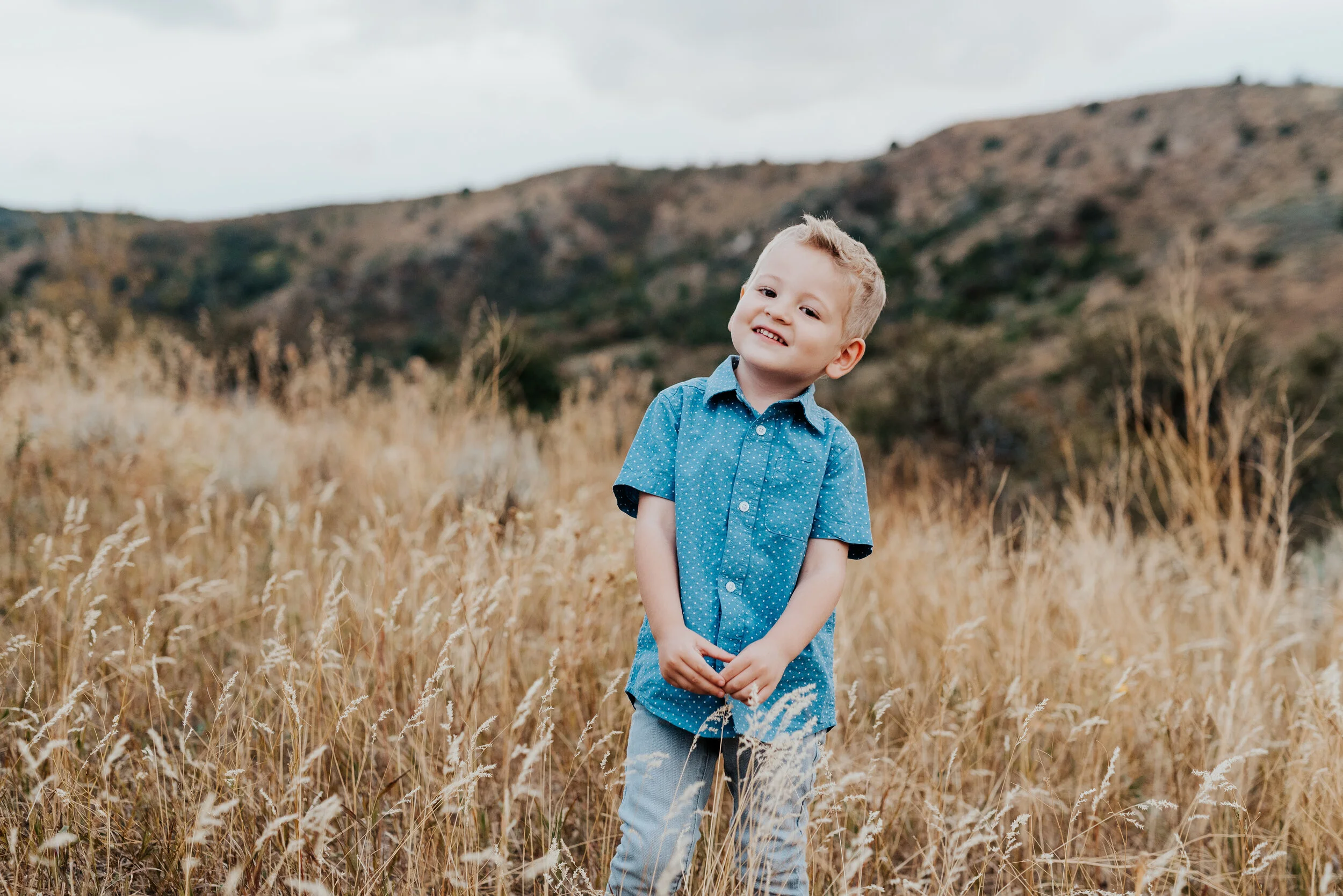 A cute little boy with blonde hair, blue eyes, and a blue shirt to match posed in a golden Cache Valley field. family pose inspiration casual outfit styles sweet parent and children poses baby announcement in family portraits in logan utah cache val…