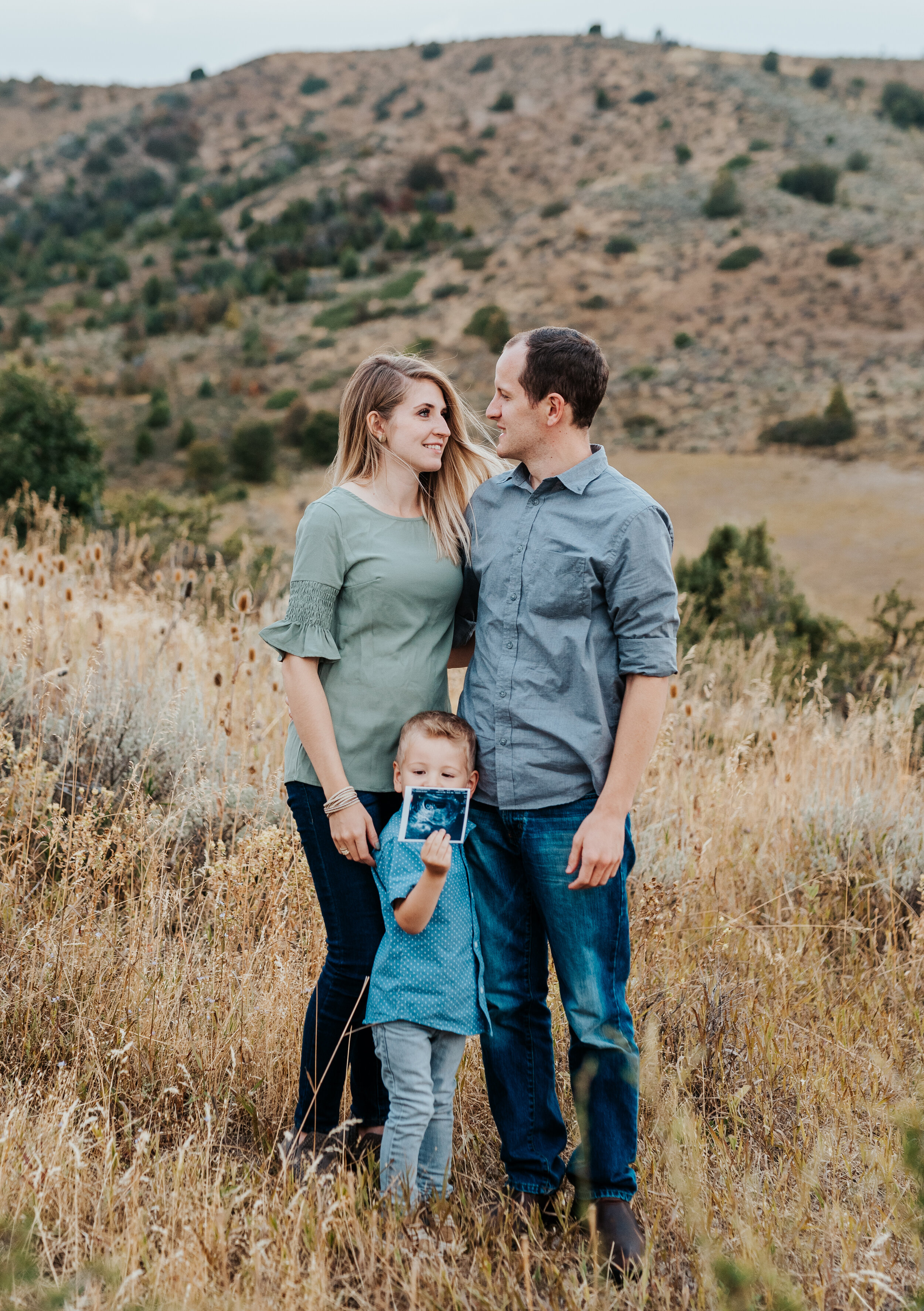  Sweet family pose with mom and dad holding their cute son close while standing in a beautiful field. natural family pose inspiration casual outfit styles sweet parent and children poses baby announcement in family portraits in logan utah cache valle