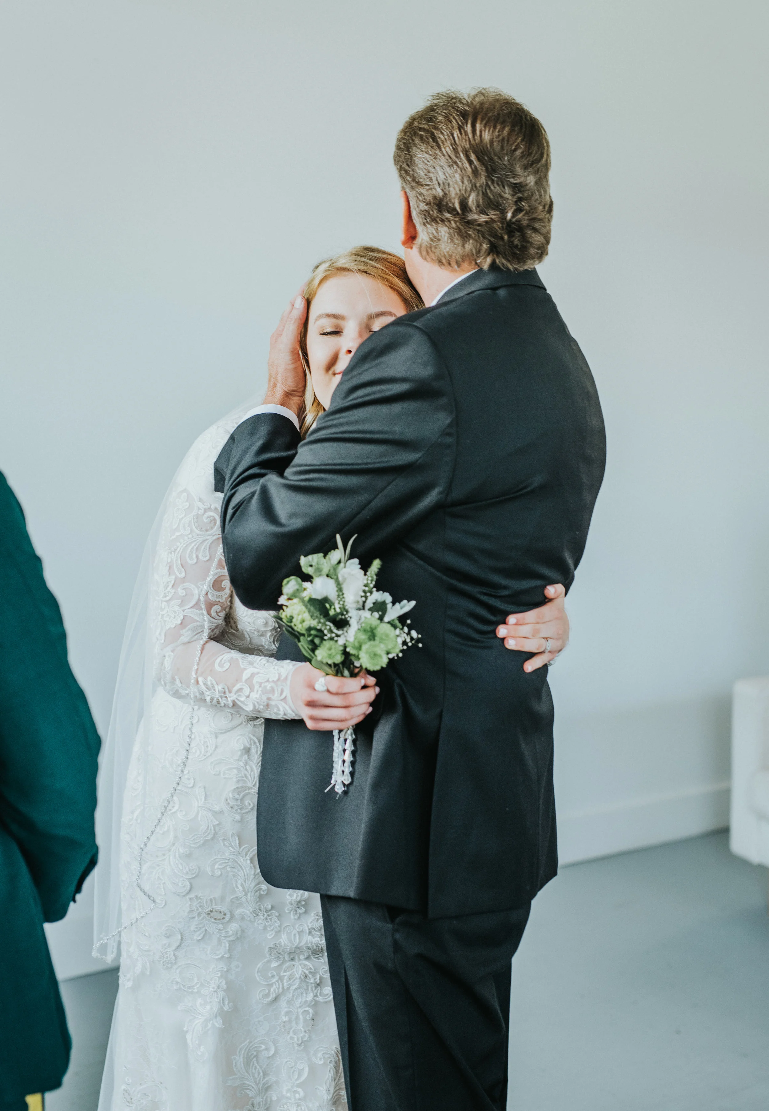  walking down the isle father of the bride hugging bride white lace modest wedding dress studio wedding ceremony professional logan utah wedding photographer happy small wildflower bouquet black wedding suit #StationStudio #WeddingCeremony #Loganutah