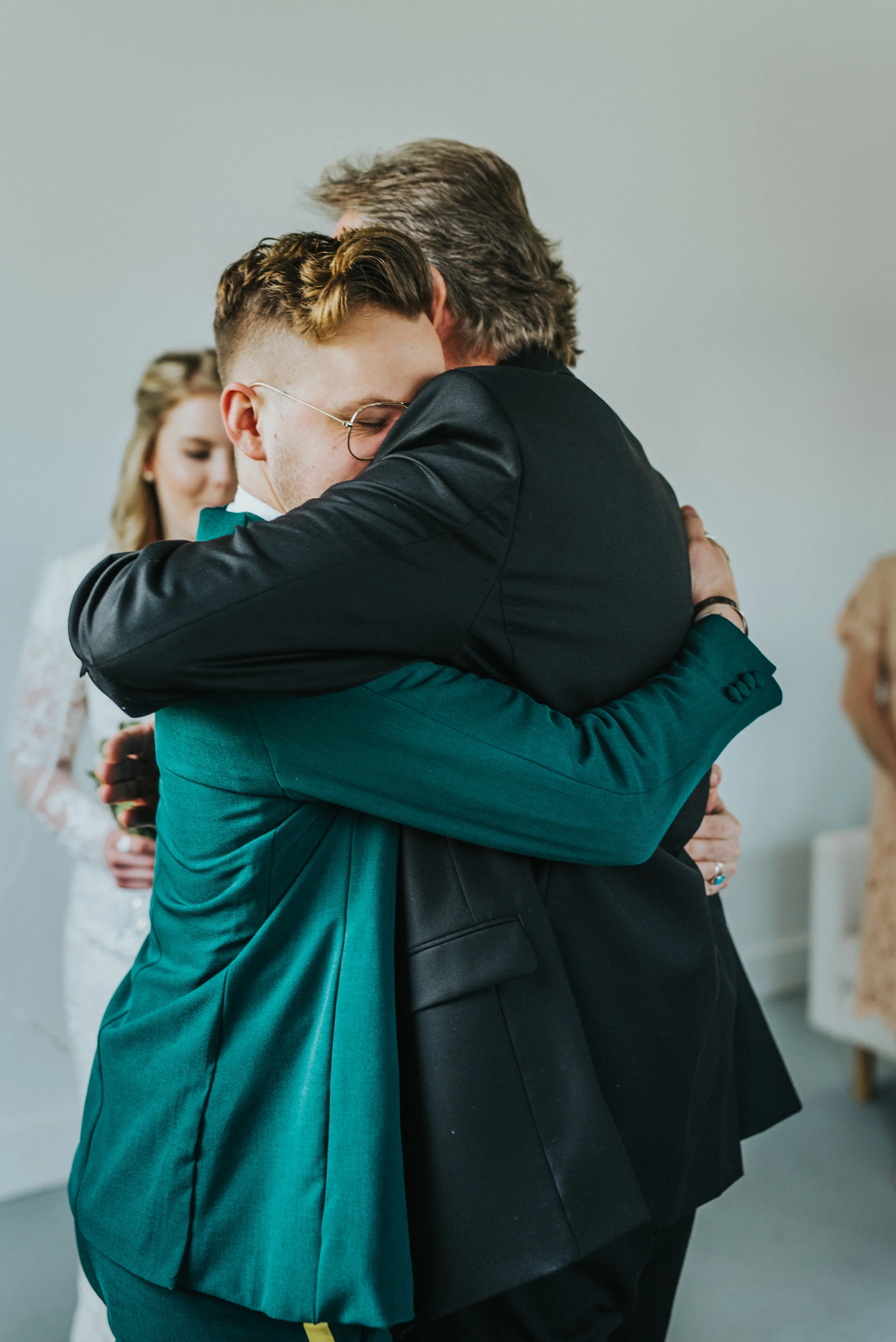  groom hugging father of the bride giving away daughter wedding studio wedding ceremony happy family emerald green retro wedding suit yellow striped pant retro glasses wedding inspiration #StationStudio #WeddingCeremony #Loganutahtemple #FreckleFarm 