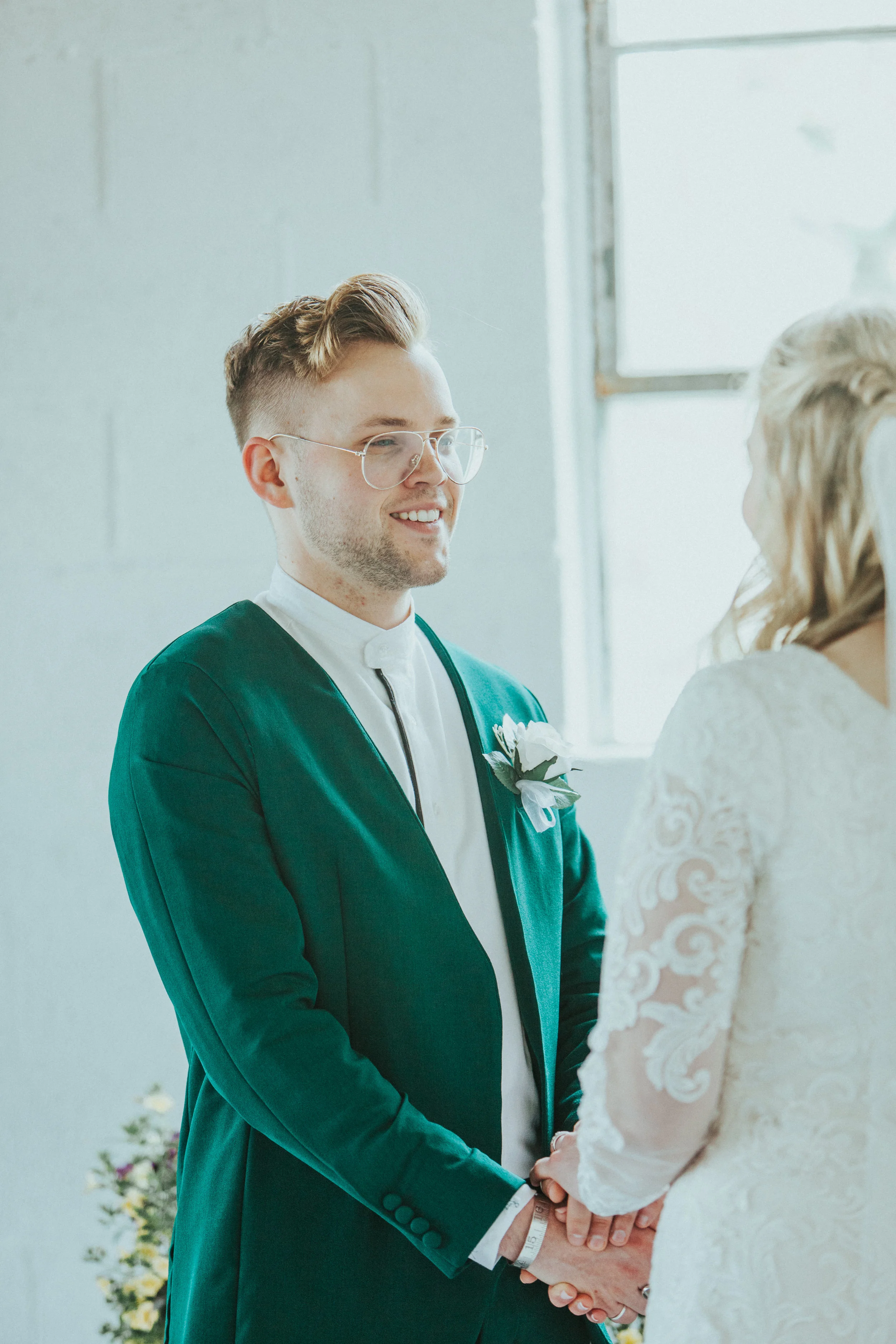  emerald green wedding suit retro wedding inspiration vintage mens glasses wedding haircut mens blonde loose wedding curls holding hands white studio wedding ceremony smiling groom long sleeved lace white wedding dress modest lds professional cache v