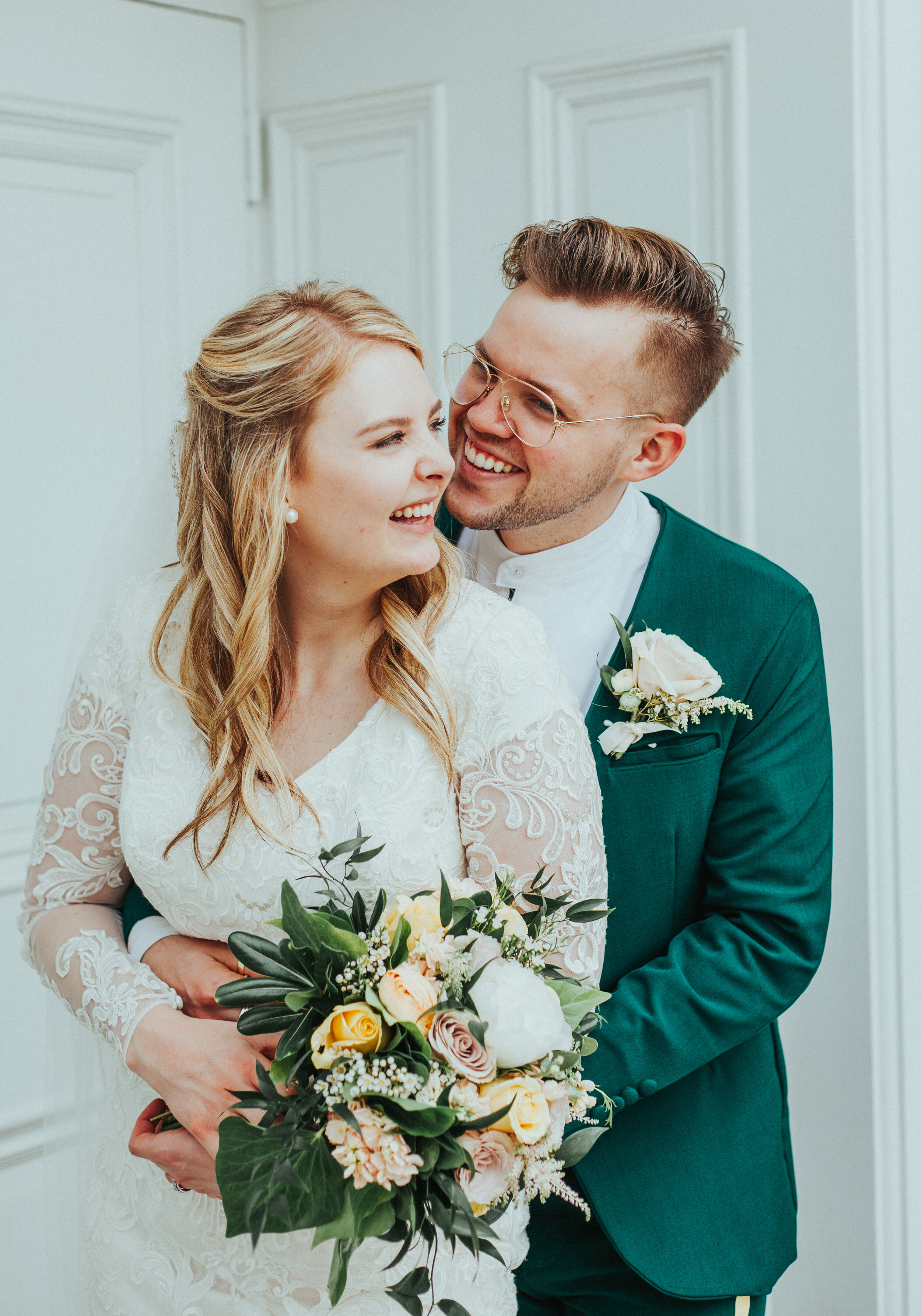  logan utah lds temple sealed for eternity white doors happy hugging playful white lace modest wedding dress emerald green retro wedding suit white and yellow bouquet boutonniere professional weddig photographer cache valley utah #StationStudio #Wedd