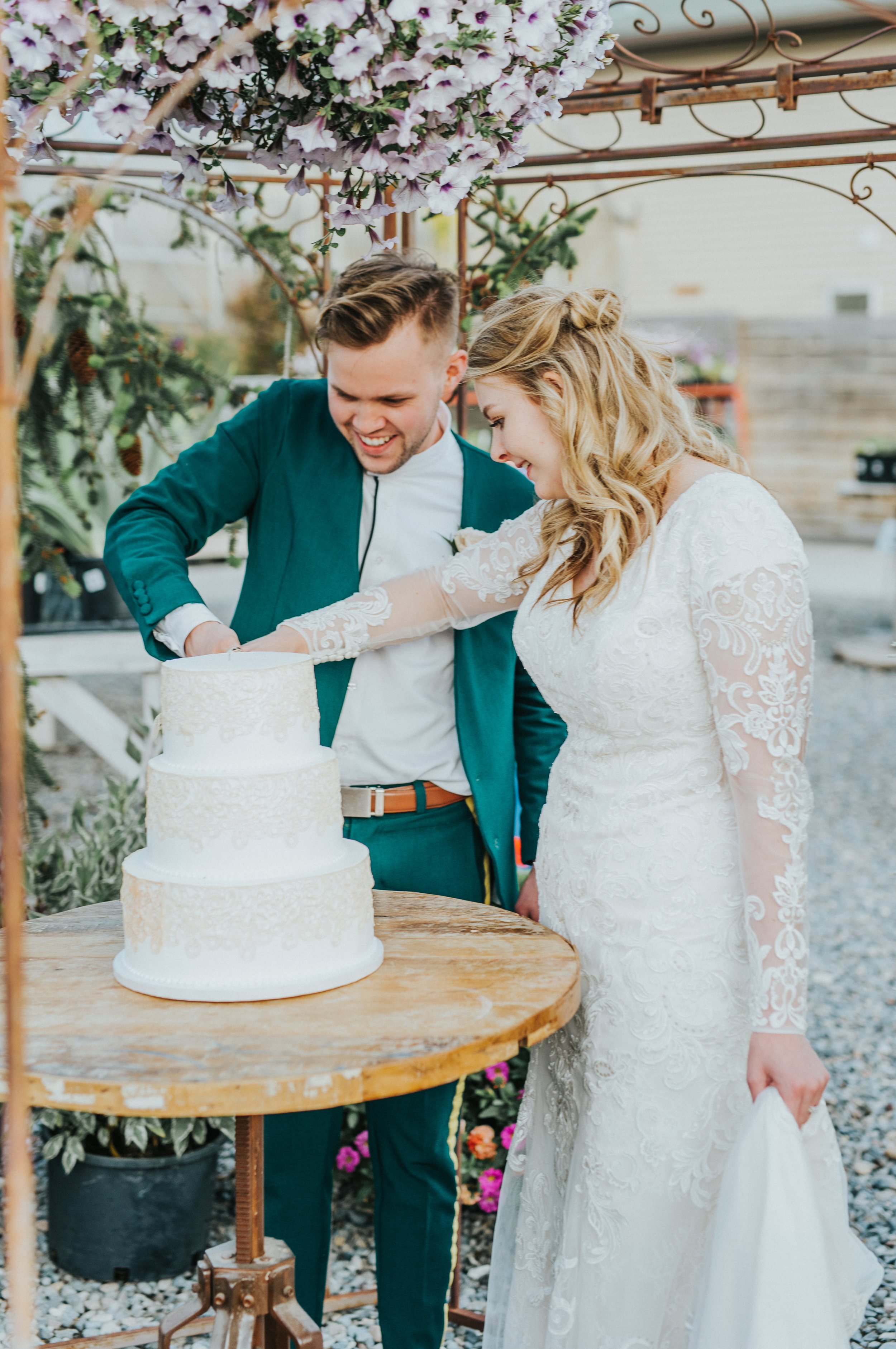  freckle farm outdoor wedding reception floral archway cutting the cake holding hands smiling lace three tiered wedding cake modest lace wedding dress half updo wedding hair retro green wedding suit professional cache valley wedding photographer #Sta