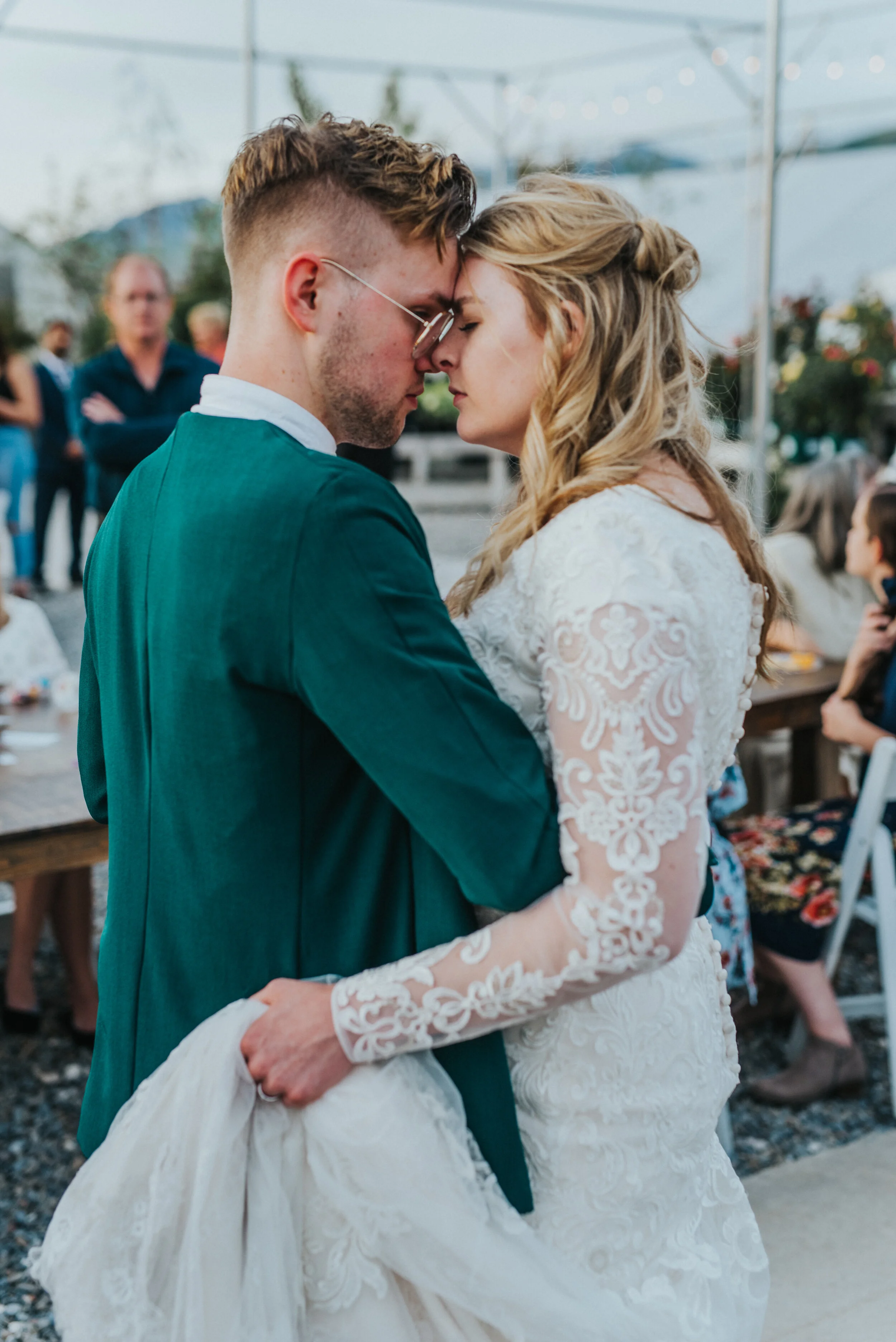  first dance string lights outdoor wedding reception hugging dancing holding wedding train modest long sleeved wedding dress lds retro green wedding suit professional logan utah wedding photographer freckle farm reception touching foreheads slow danc