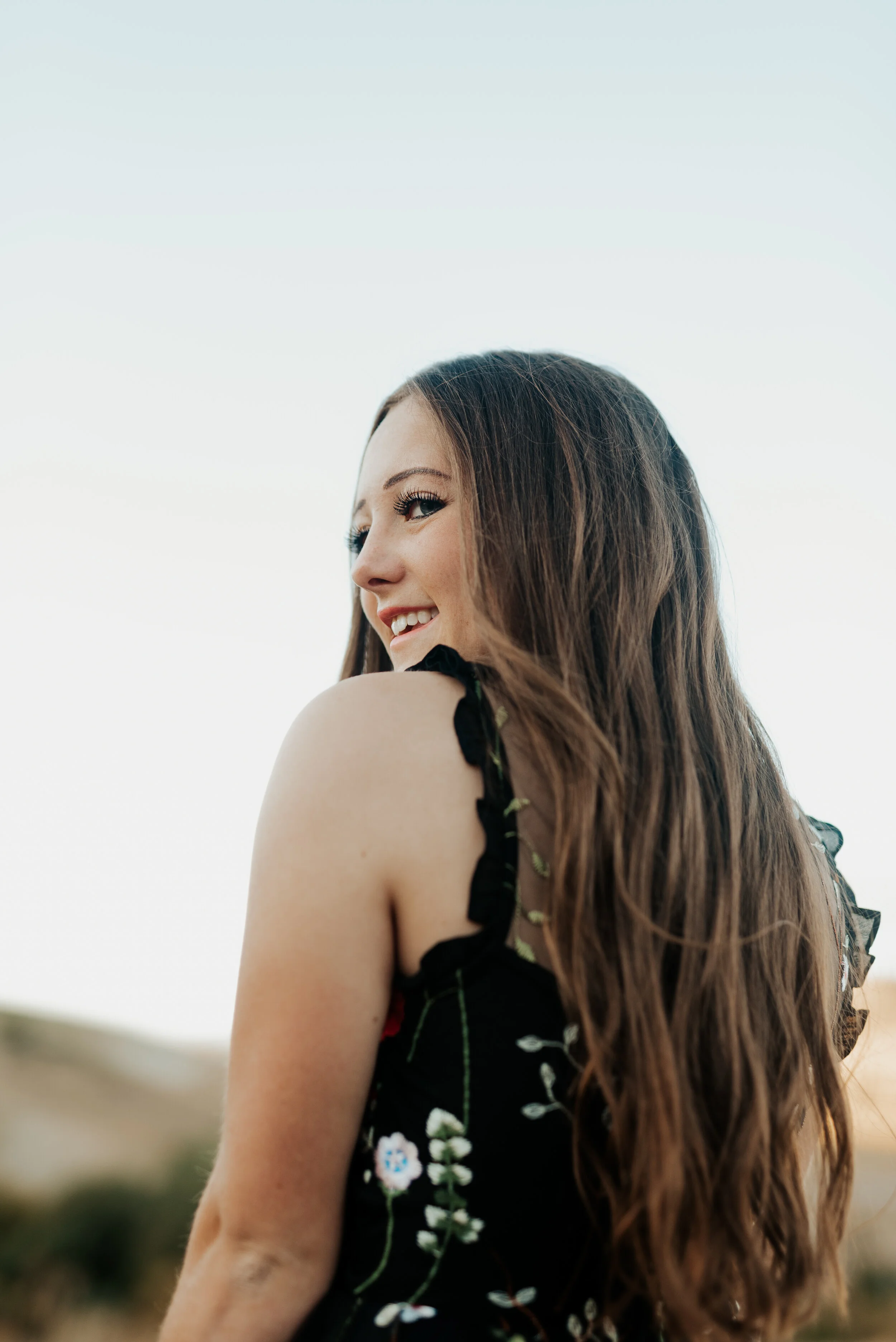  Brunette girl with long hair looking over her shoulder in a black flutter sleeve dress. senior photo poses logan utah photographers teen fashion senior pictures photo session outfit inspiration casual senior picture outfits senior in high school gra