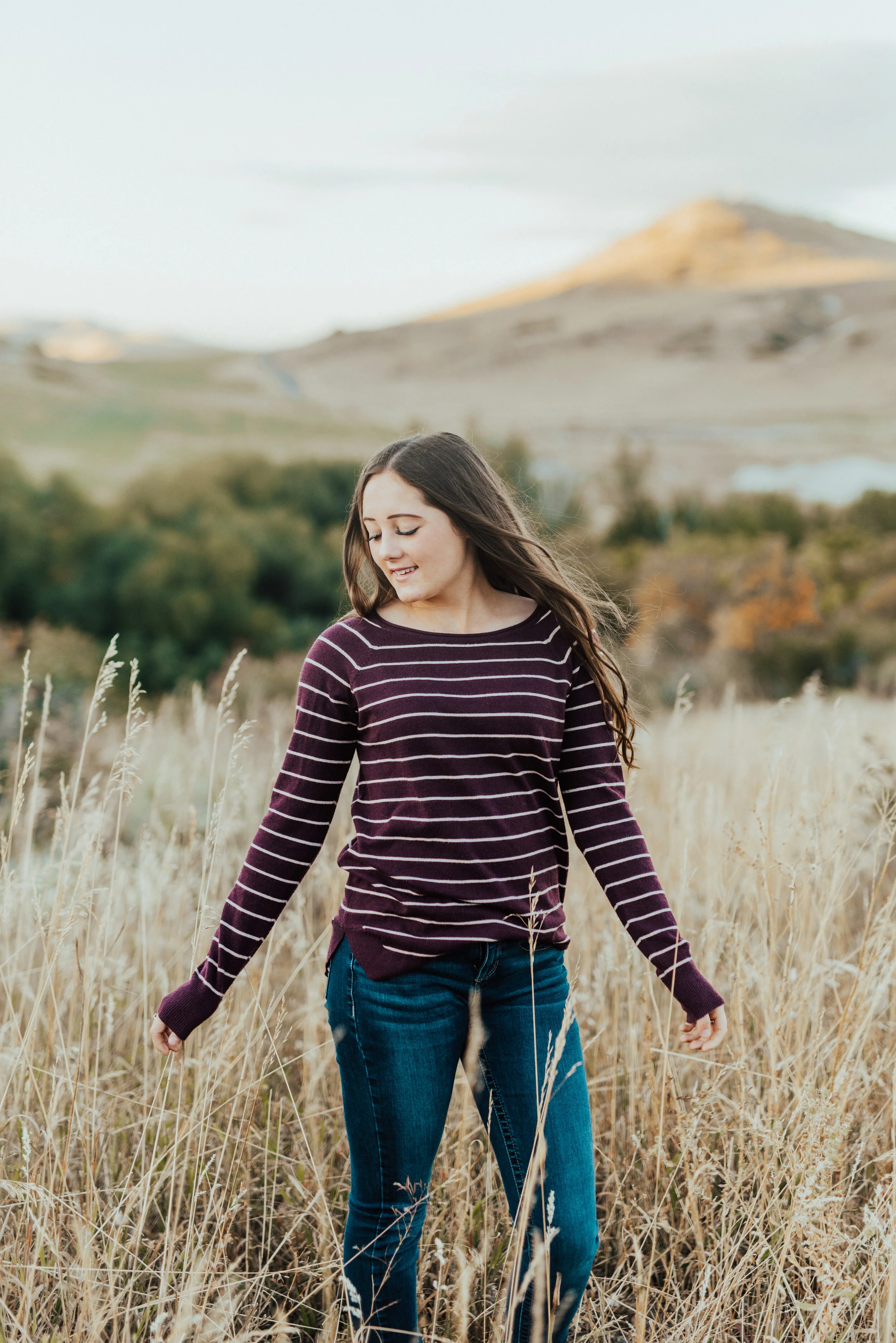  Teen girl in jeans and a burgundy striped sweater standing in a beautiful field. cache valley senior photo poses logan utah photographers teen fashion senior pictures photo session outfit inspiration casual senior picture outfits senior in high scho