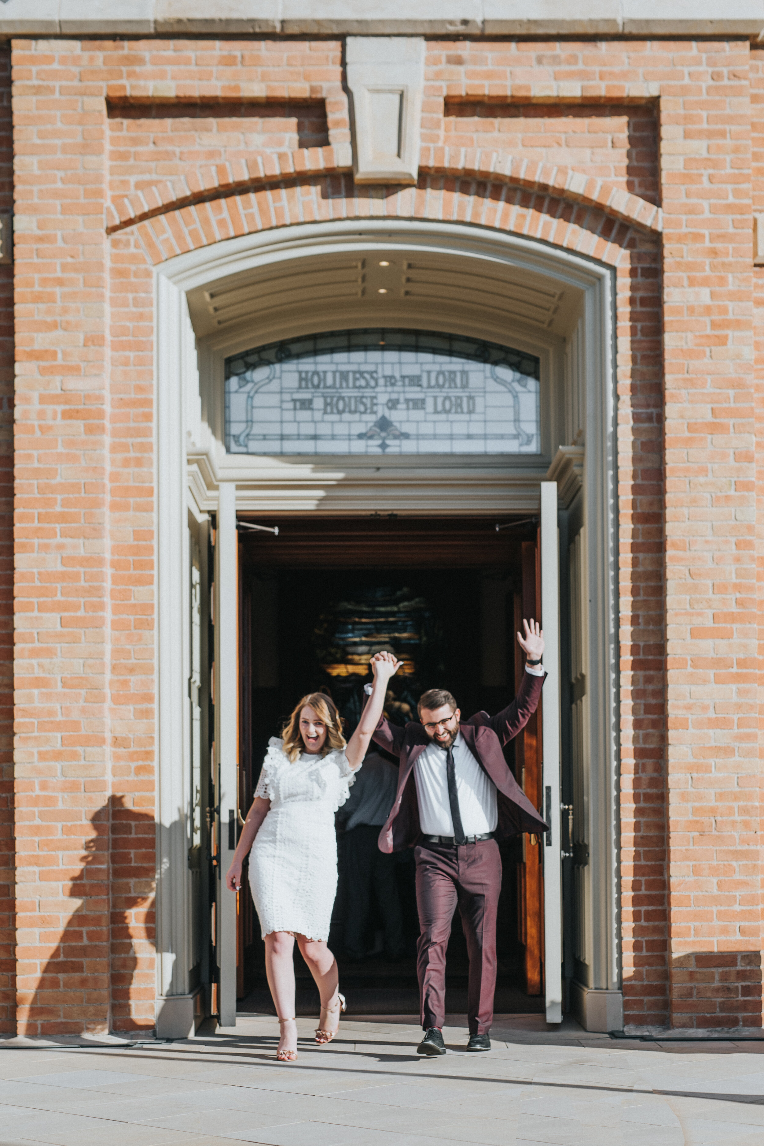  provo city center temple exit celebration hands in the air smiling happy burgundy grooms suit knee length lace wedding dress professional wedding photographer utah valley provo utah holding hands just married #utahvalleyweddingphotographer #provophotographer #provoutah #provocitycentertemple #lds #weddinginspo #ido #shesaidyes #utah #professionalweddingphotographer  