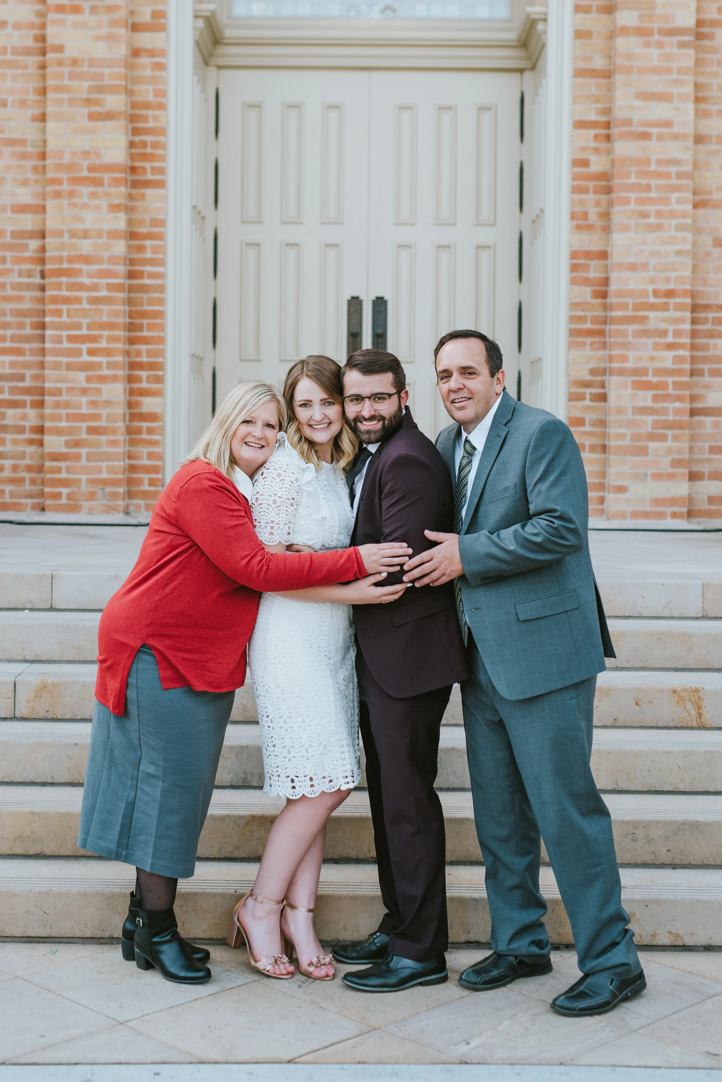  mother of the groom, father of the groom provo city center temple wedding provo utah wedding photography utah valley photographer hugging smiling happy wedding day burgundy wedding suit knee length modest lace wedding dress #utahvalleyweddingphotogr